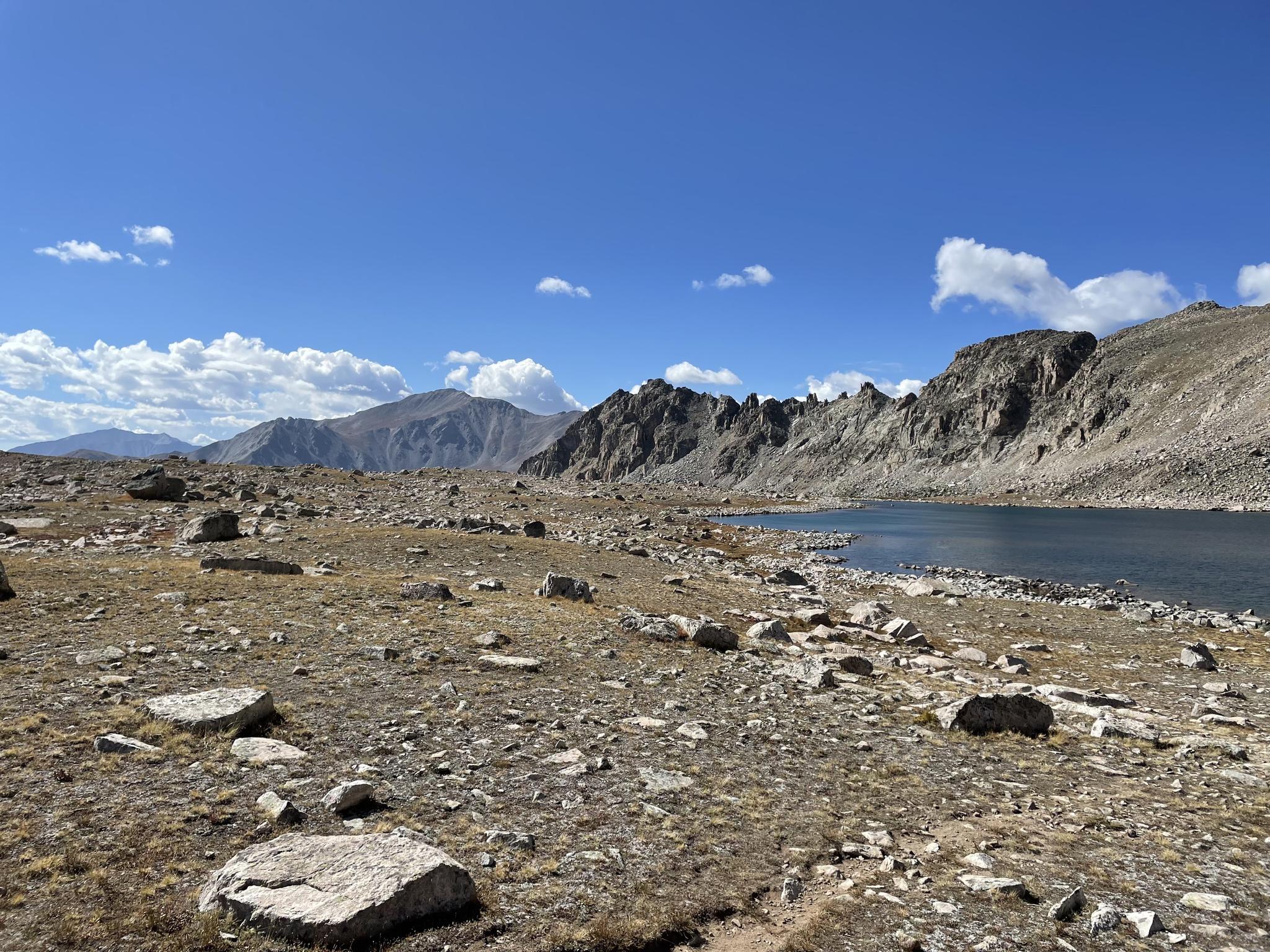 A rocky, barren landscape with a dark blue lake and distant mountains.