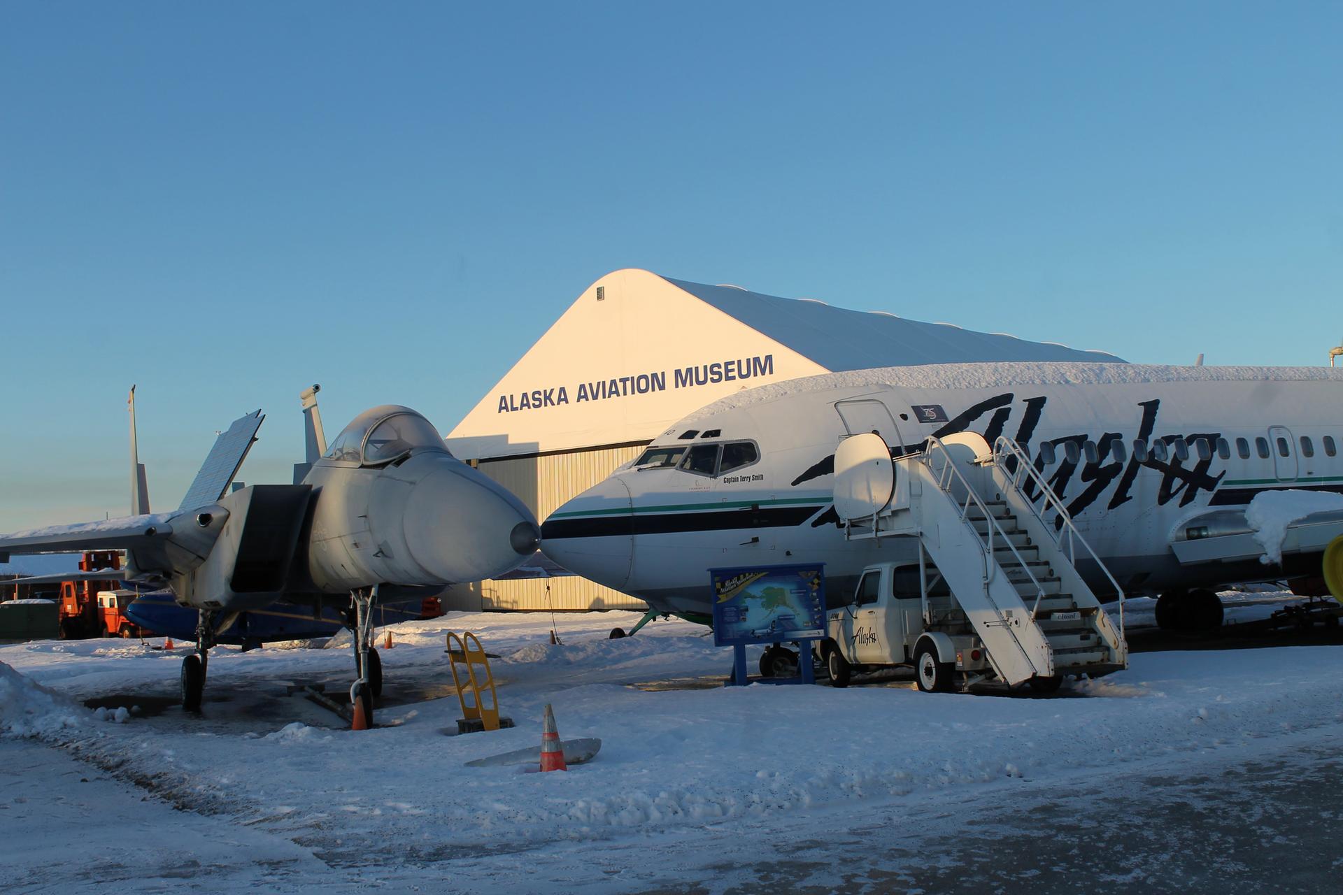 Two large airplanes on snowy ground in front of a white building.
