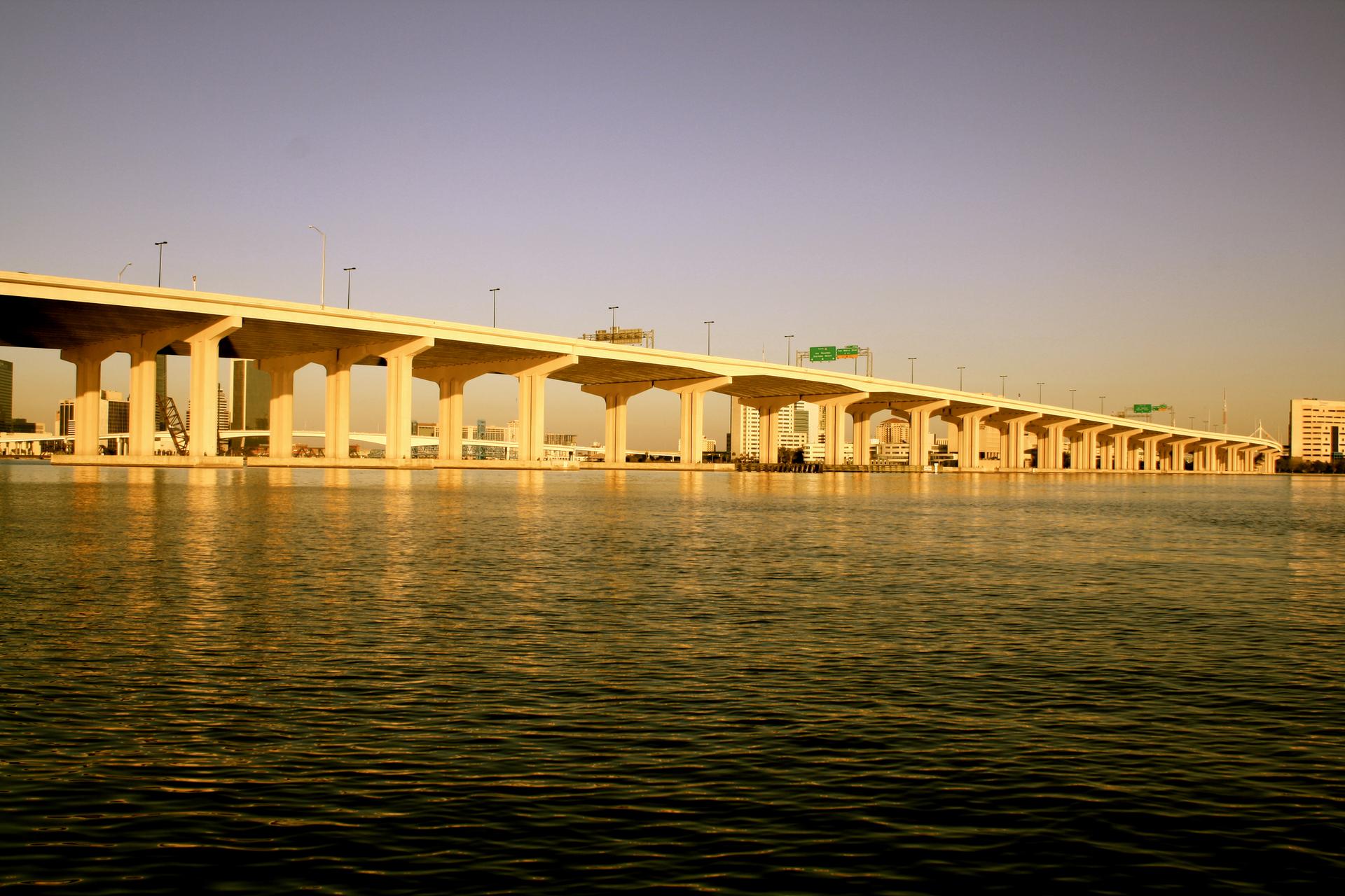 Long concrete bridge spanning a wide river under warm, golden light.