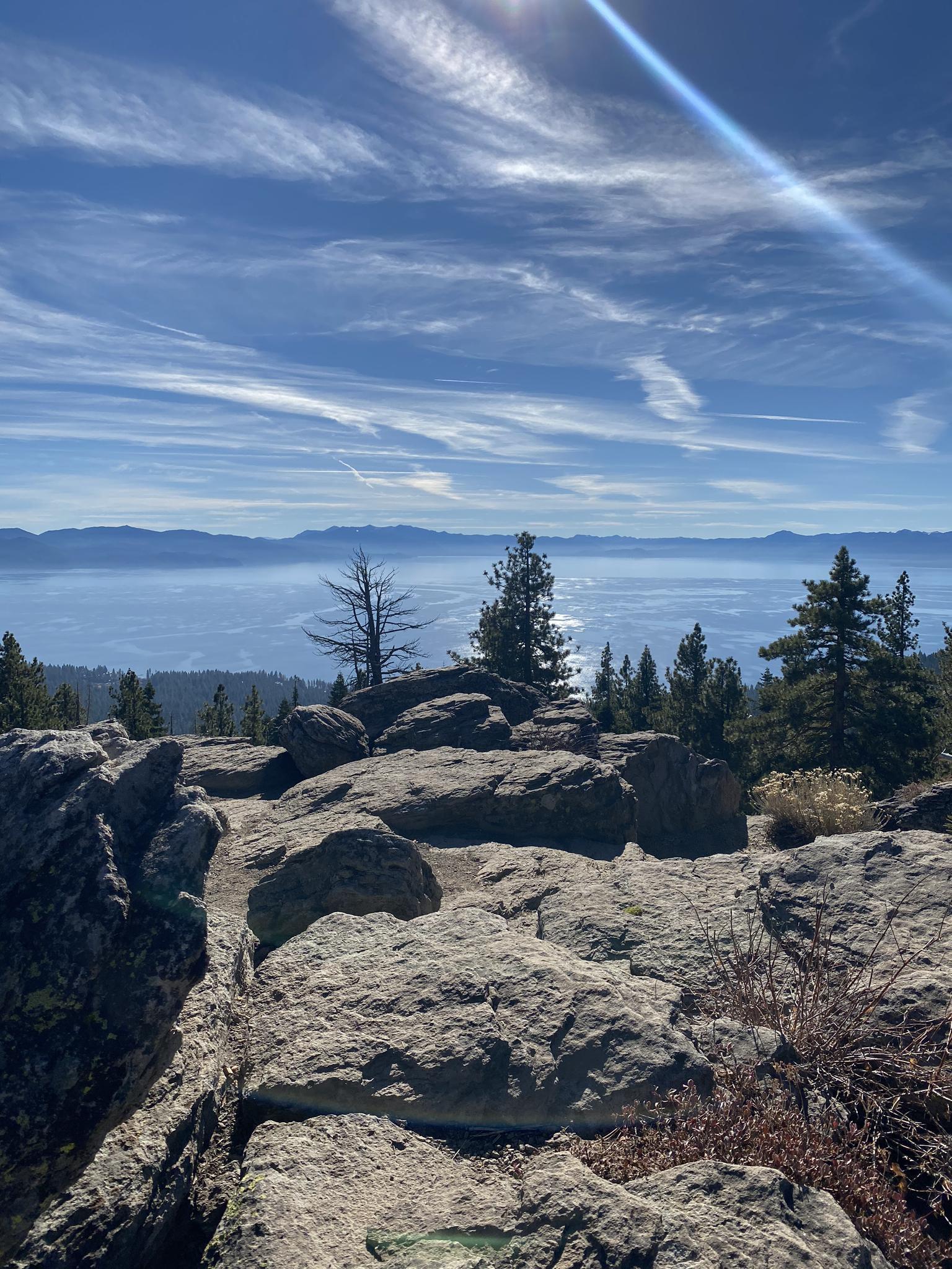 Rocky mountain top view of a hazy lake and distant mountains, bright sun.