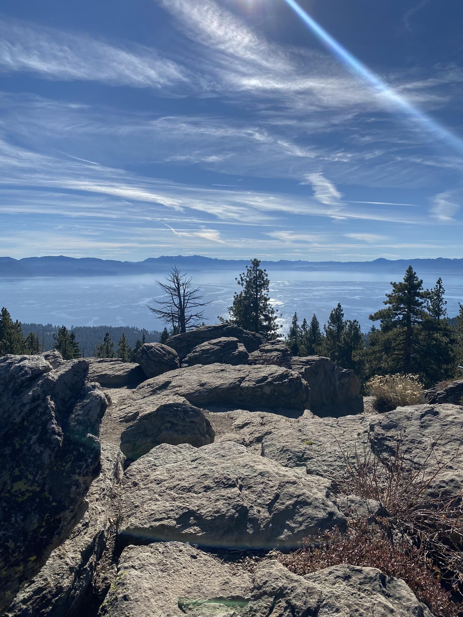Rocky mountain top view of a hazy lake and distant mountains, bright sun. - Tahoe Rim Trail to Picnic Rock Viewpoint