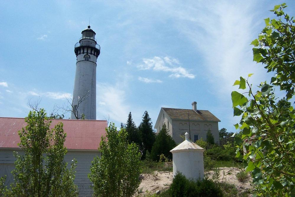 A tall white lighthouse and buildings on a sandy hill under a bright sky.