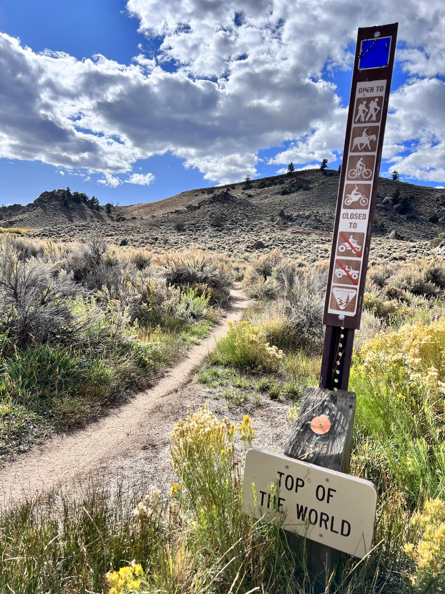 Trail sign indicating "Top of the World" next to a dirt path.