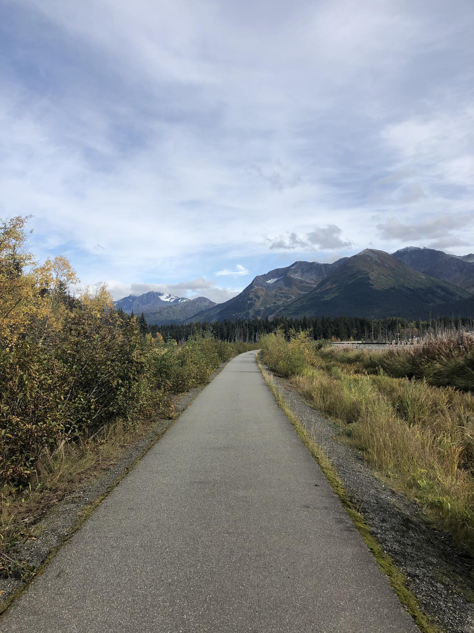 Paved path leading towards distant mountains under a cloudy sky.