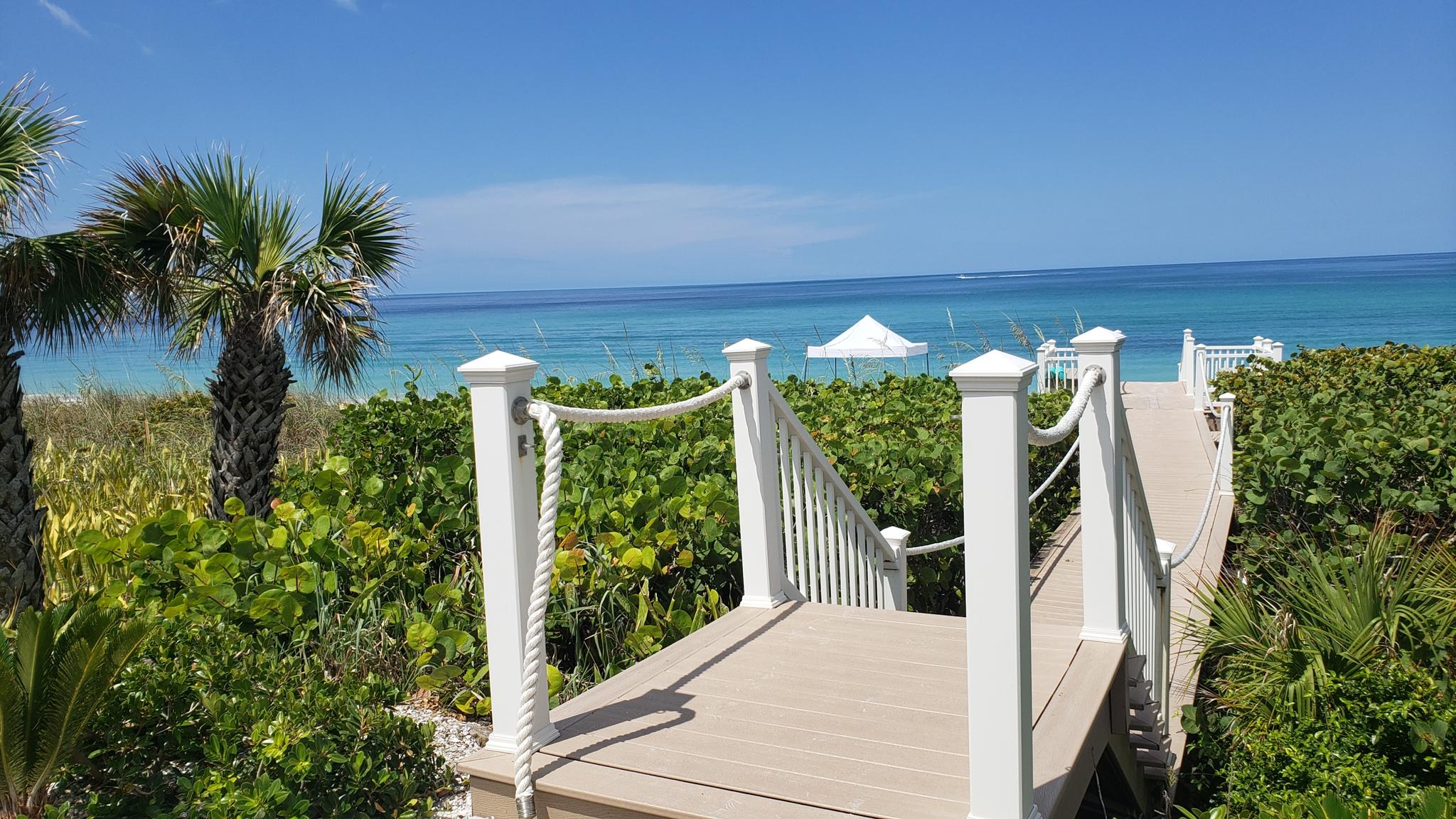 Boardwalk leads to a sunny beach with palm trees and turquoise ocean.