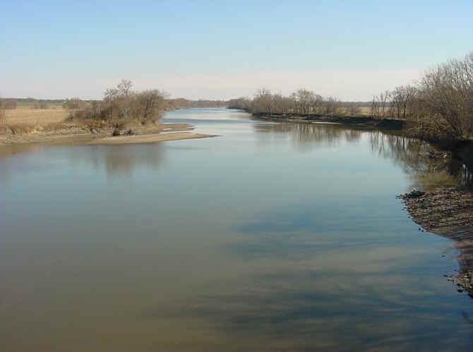 Wide river flowing between banks with bare trees under a clear sky.