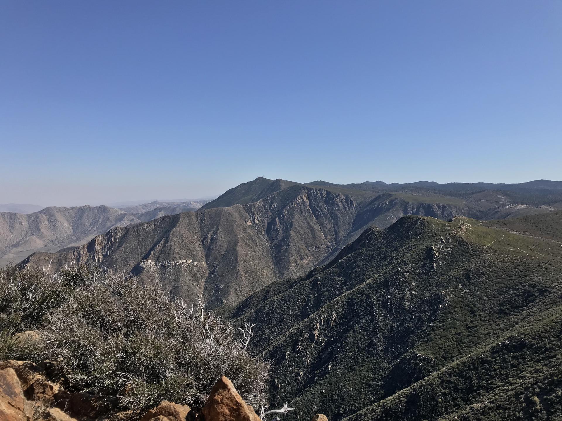 Vast mountain range with rugged, vegetated peaks under a clear blue sky.