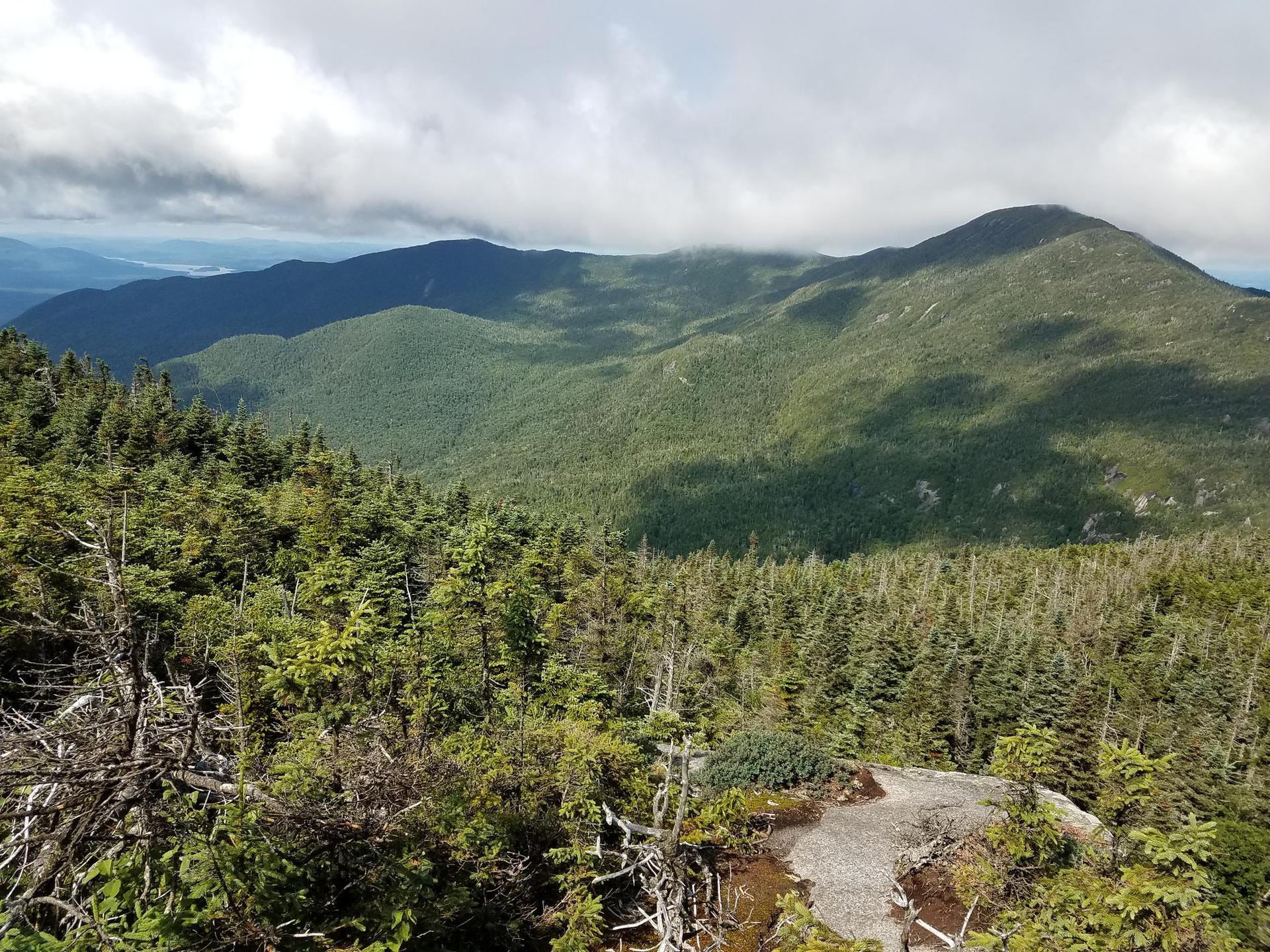 Vast forested mountains under a partly cloudy sky with sun and shadows.
