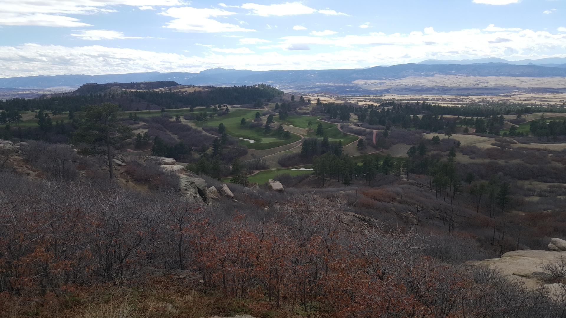 Panoramic view of a golf course winding through rocky hills under a cloudy sky.
