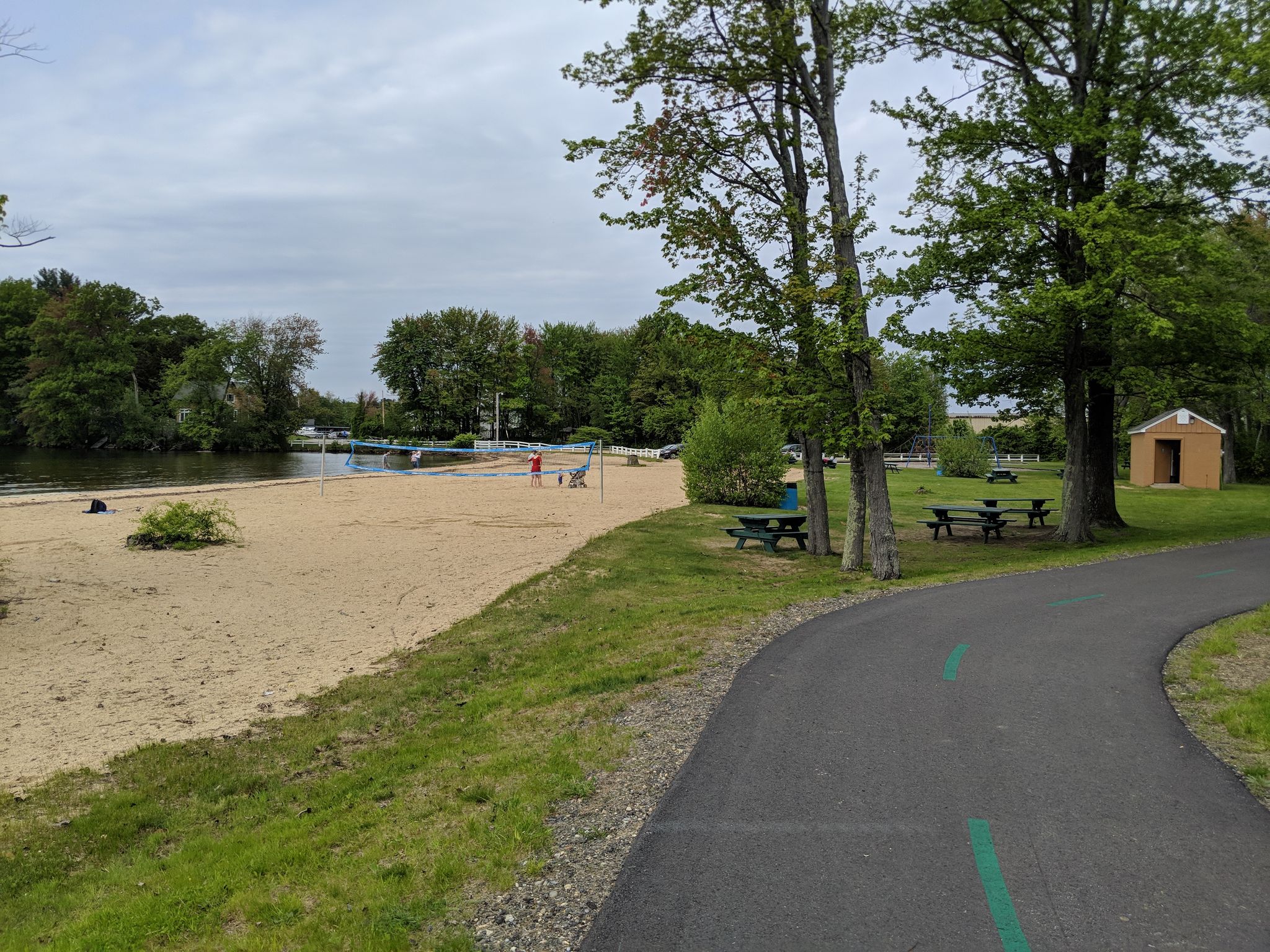 Sandy beach by a lake, with a paved path and picnic tables. - WOW and Winni Trail