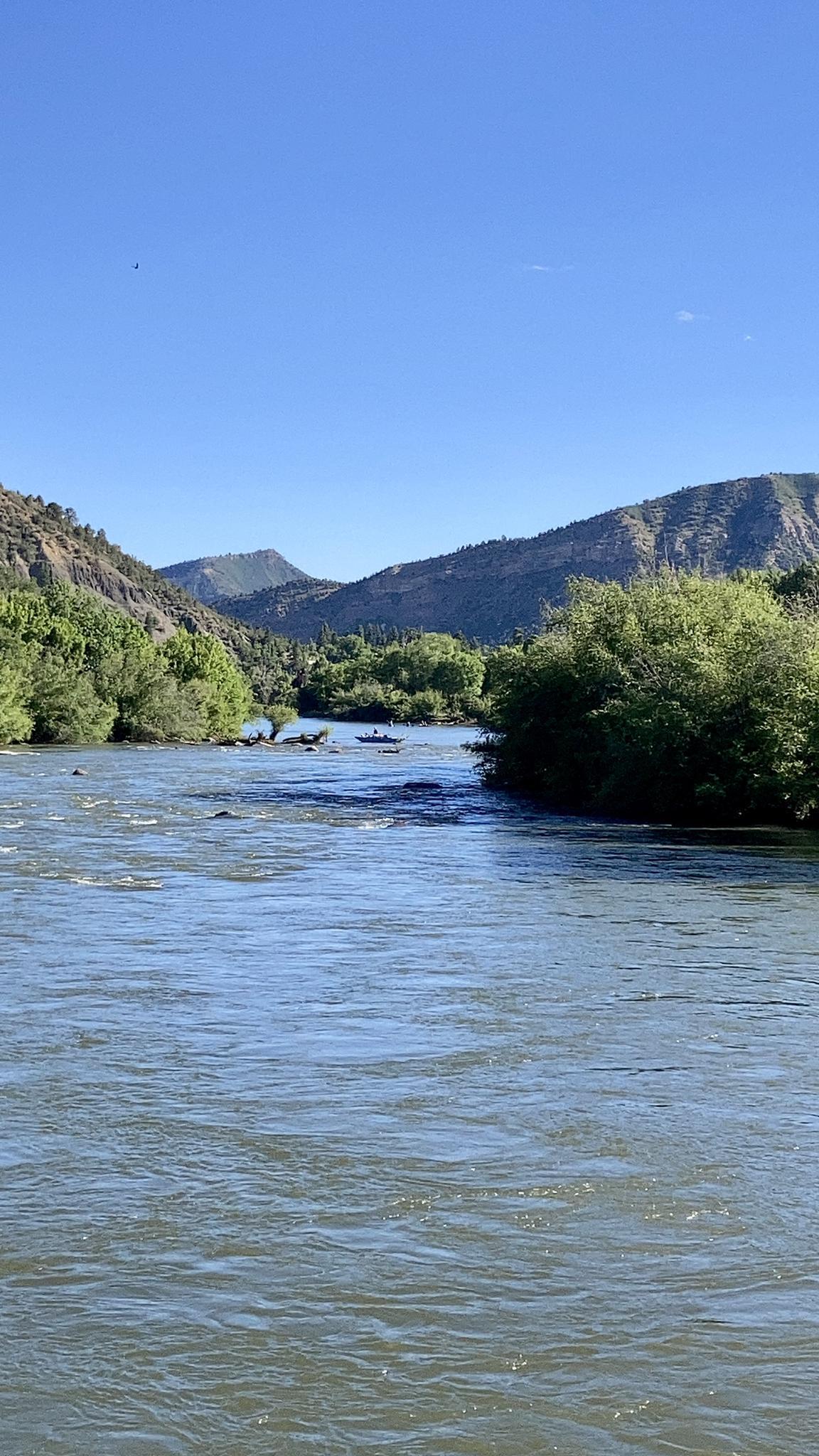 A wide river flows through a green valley with mountains under a clear sky.