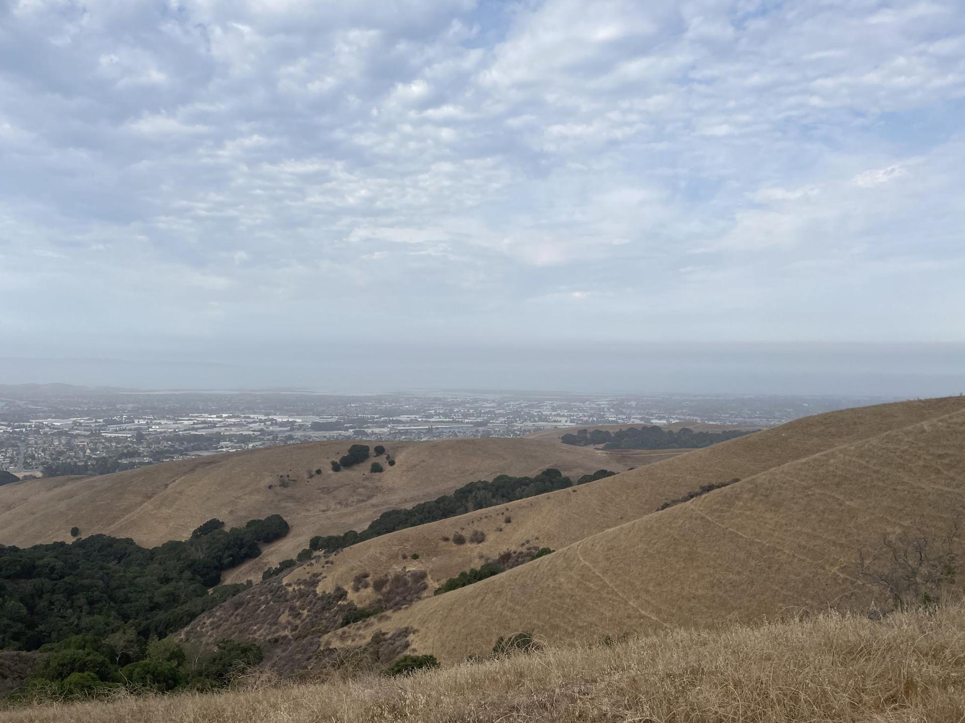 Hazy view of dry hills and a distant city under a cloudy sky.