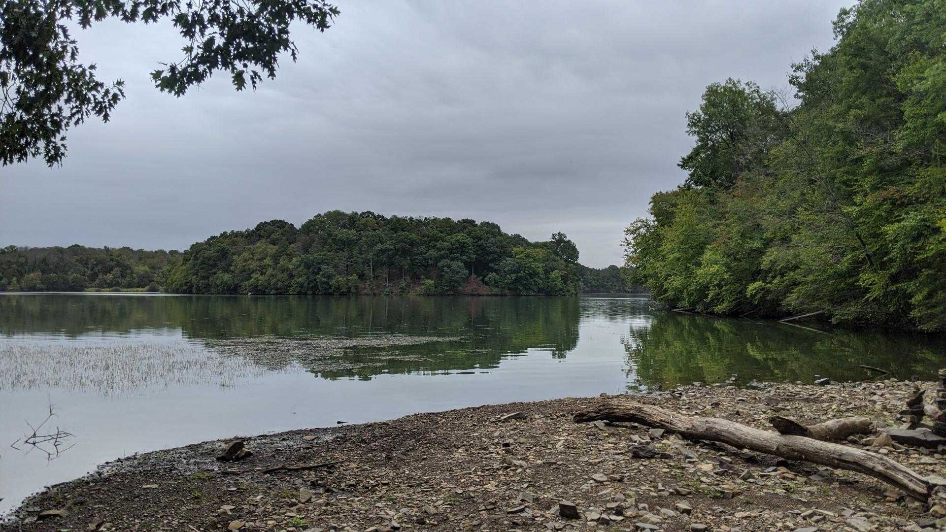 Overcast day over a lake with green trees and a rocky shore.