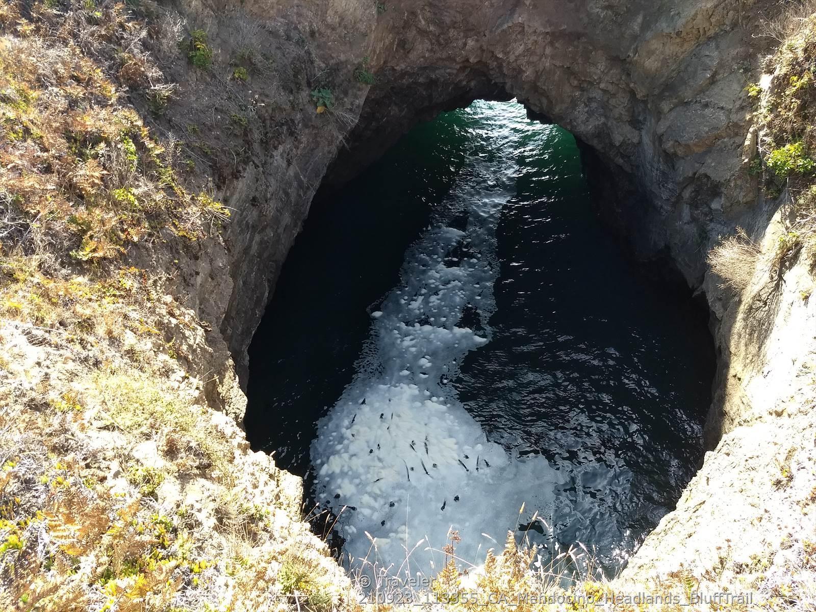 Turbulent ocean water flowing into a dark, rocky sea cave from above.