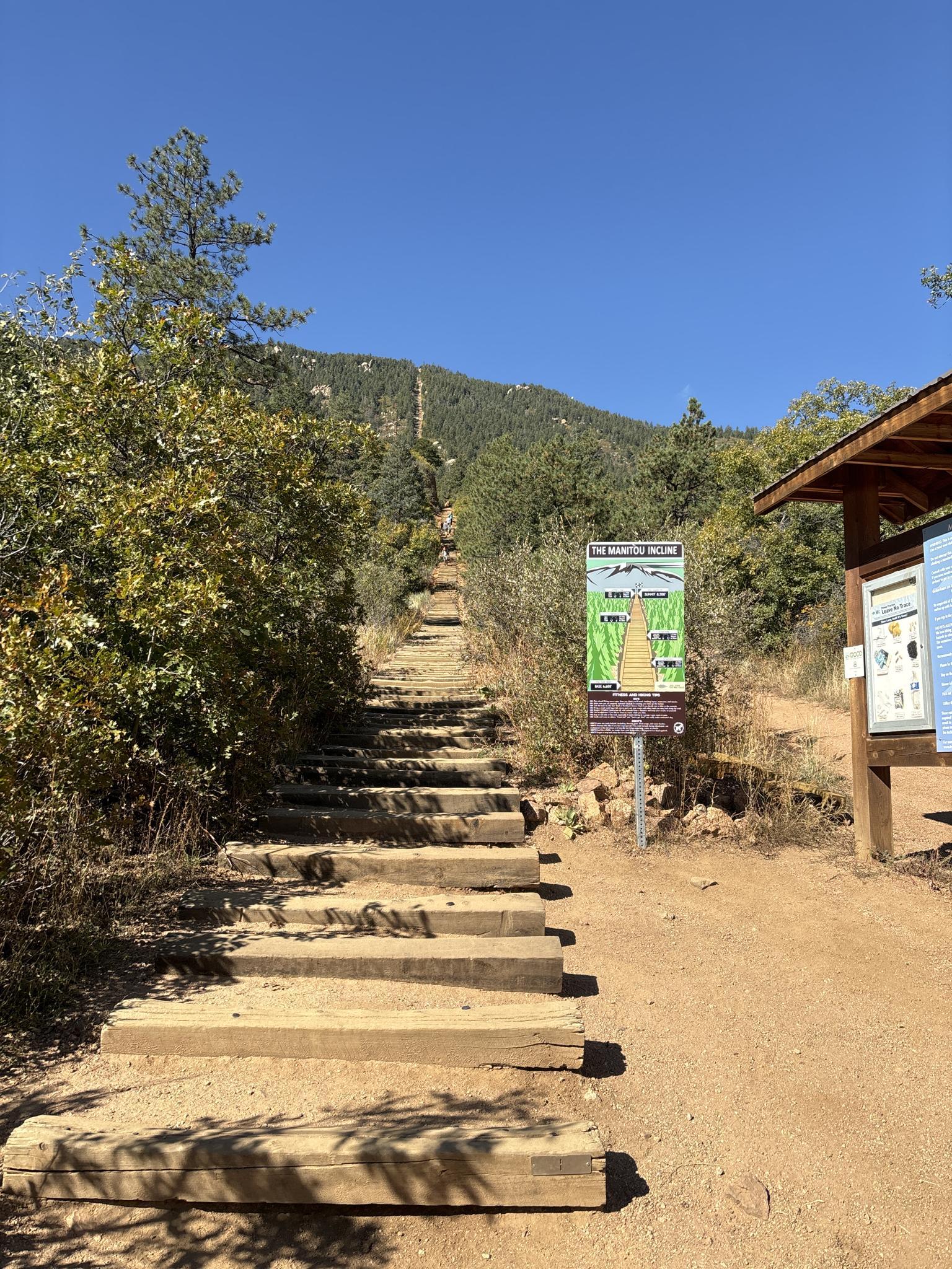 Long wooden staircase ascending a sunny mountain, with a trail sign.