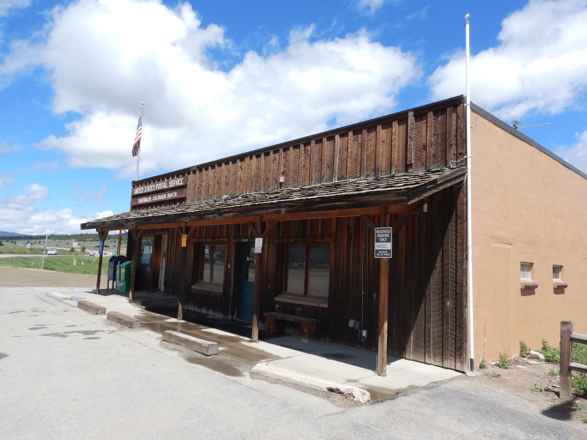A rustic wooden building with a flag under a bright, partly cloudy sky. - Tabernash loop