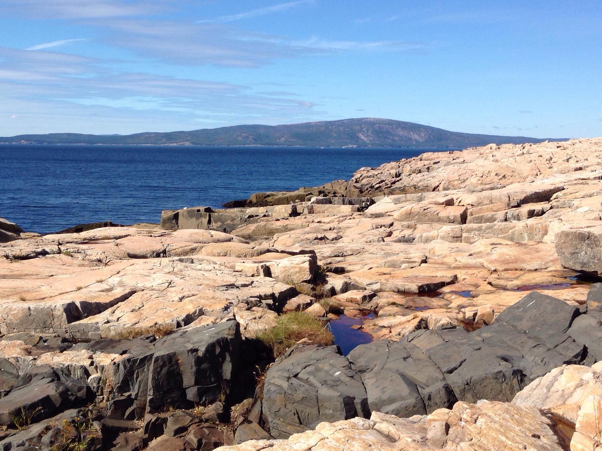 Bright sun illuminates rugged coastal cliffs overlooking a vast blue ocean.