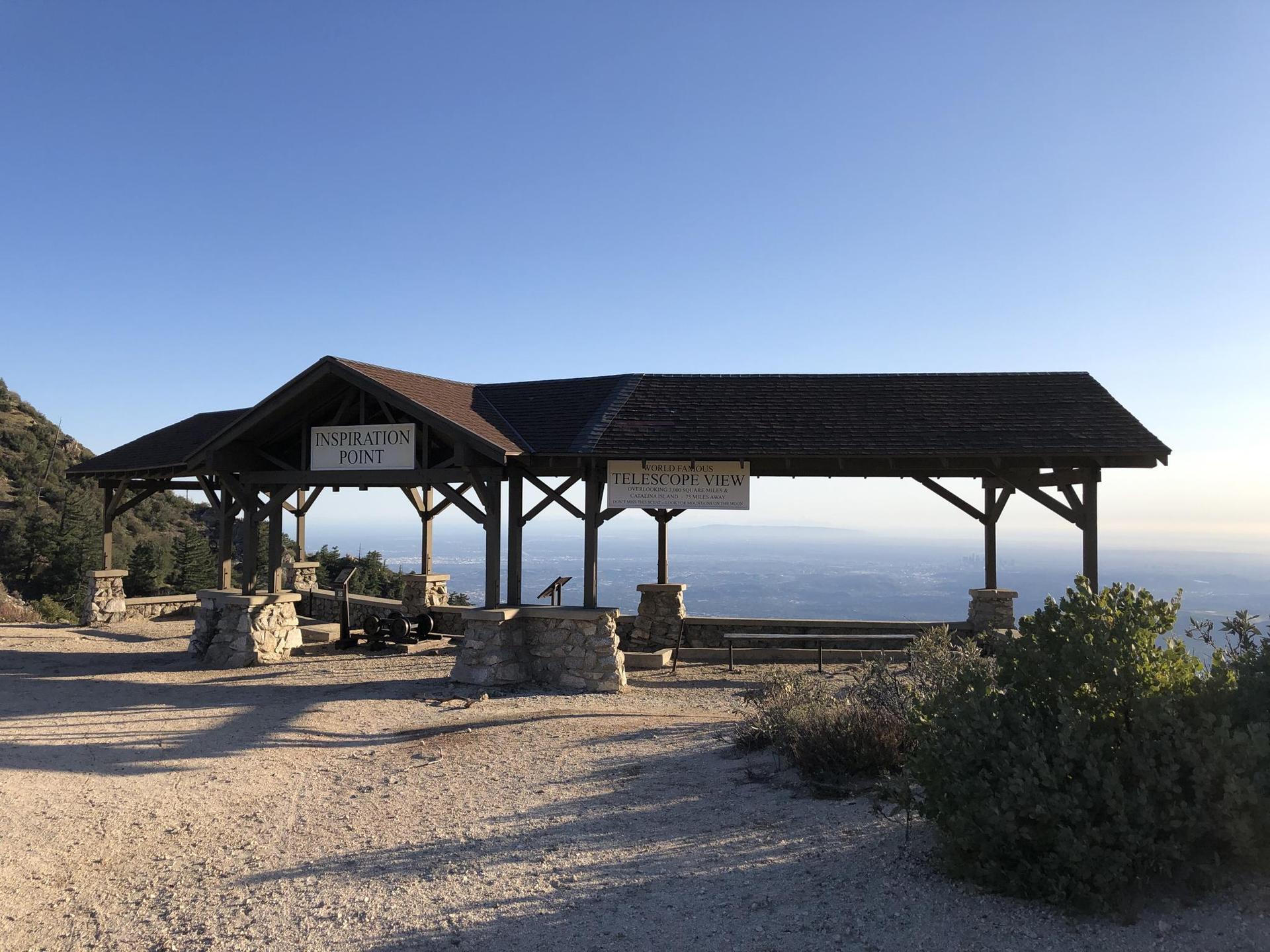 A large wooden pavilion overlooks a hazy distant view under a clear, sunny sky.