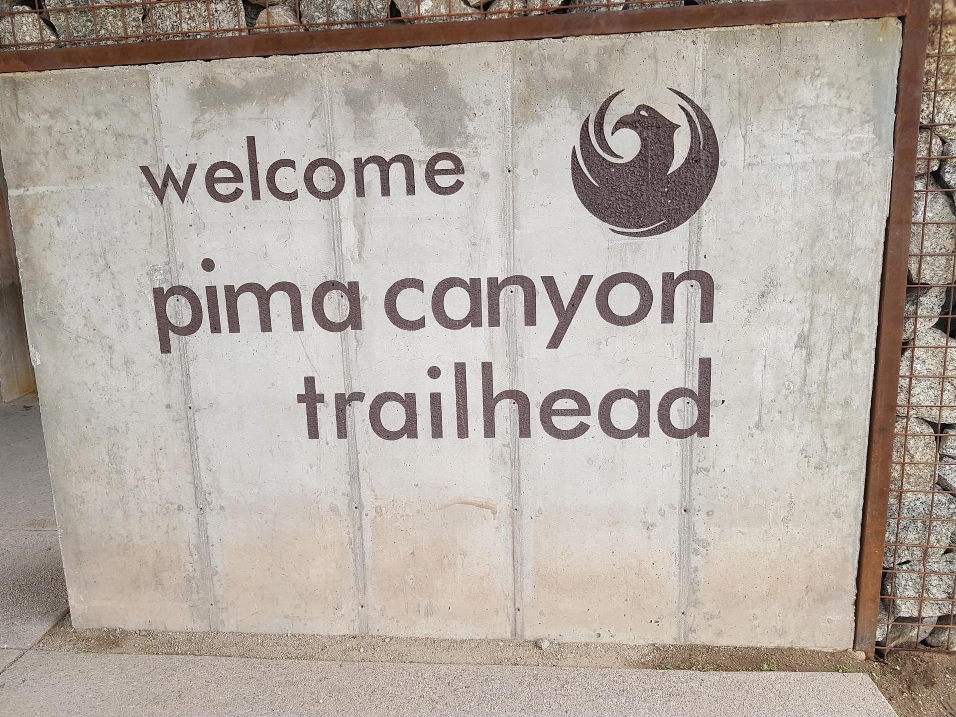 Concrete sign with 'welcome pima canyon trailhead' and a bird logo.