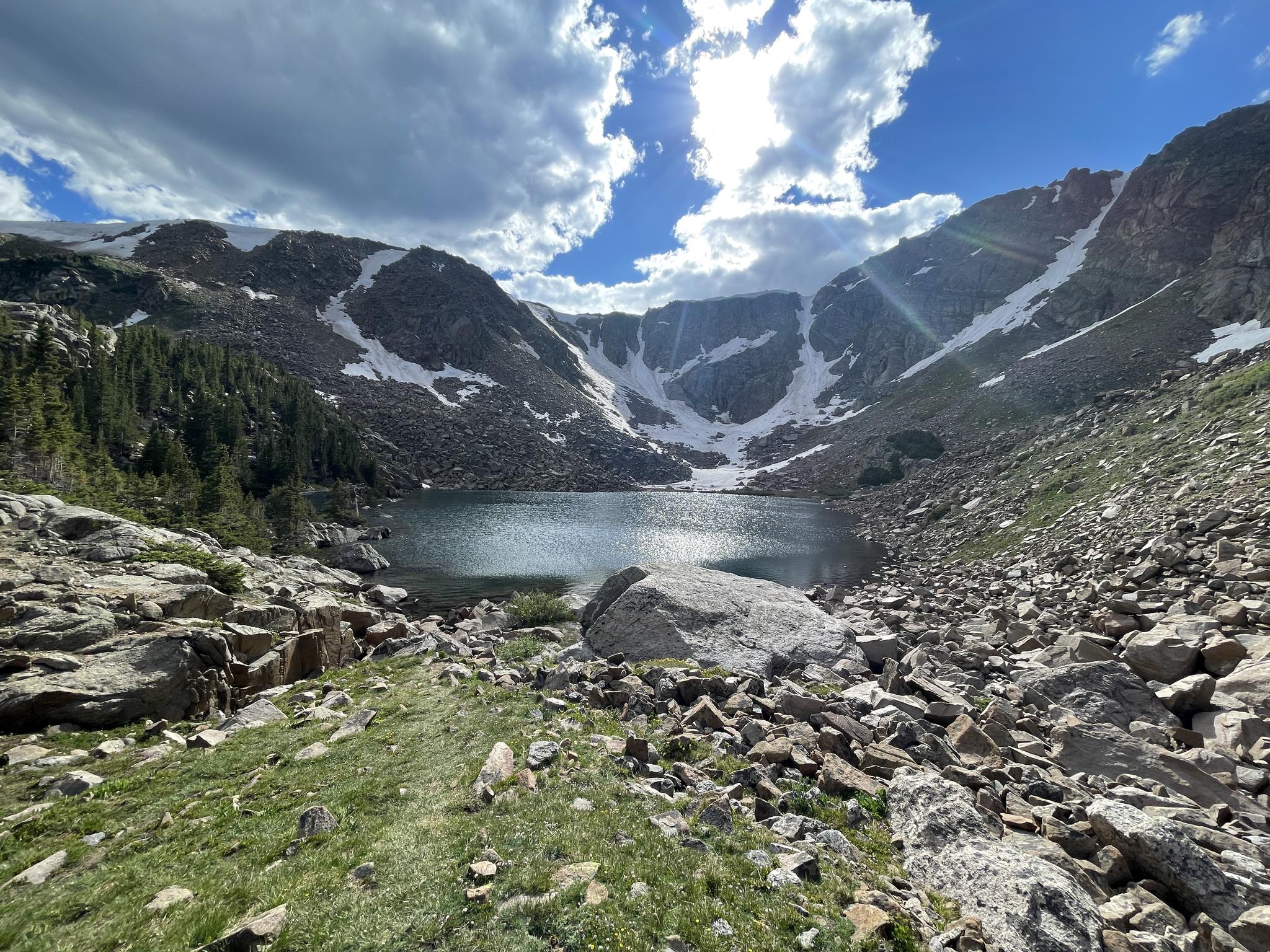 Mountain lake nestled in a rocky basin with snowy slopes and bright sun.