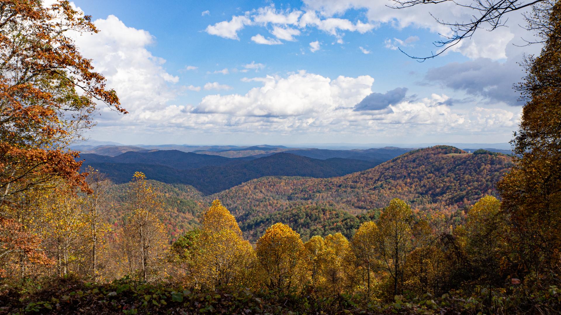 Vast autumn mountain landscape under a bright, partly cloudy sky.