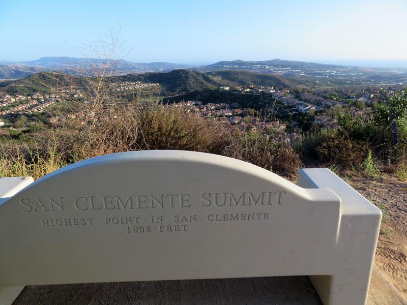 A stone bench overlooks a vast hilly landscape and distant homes.