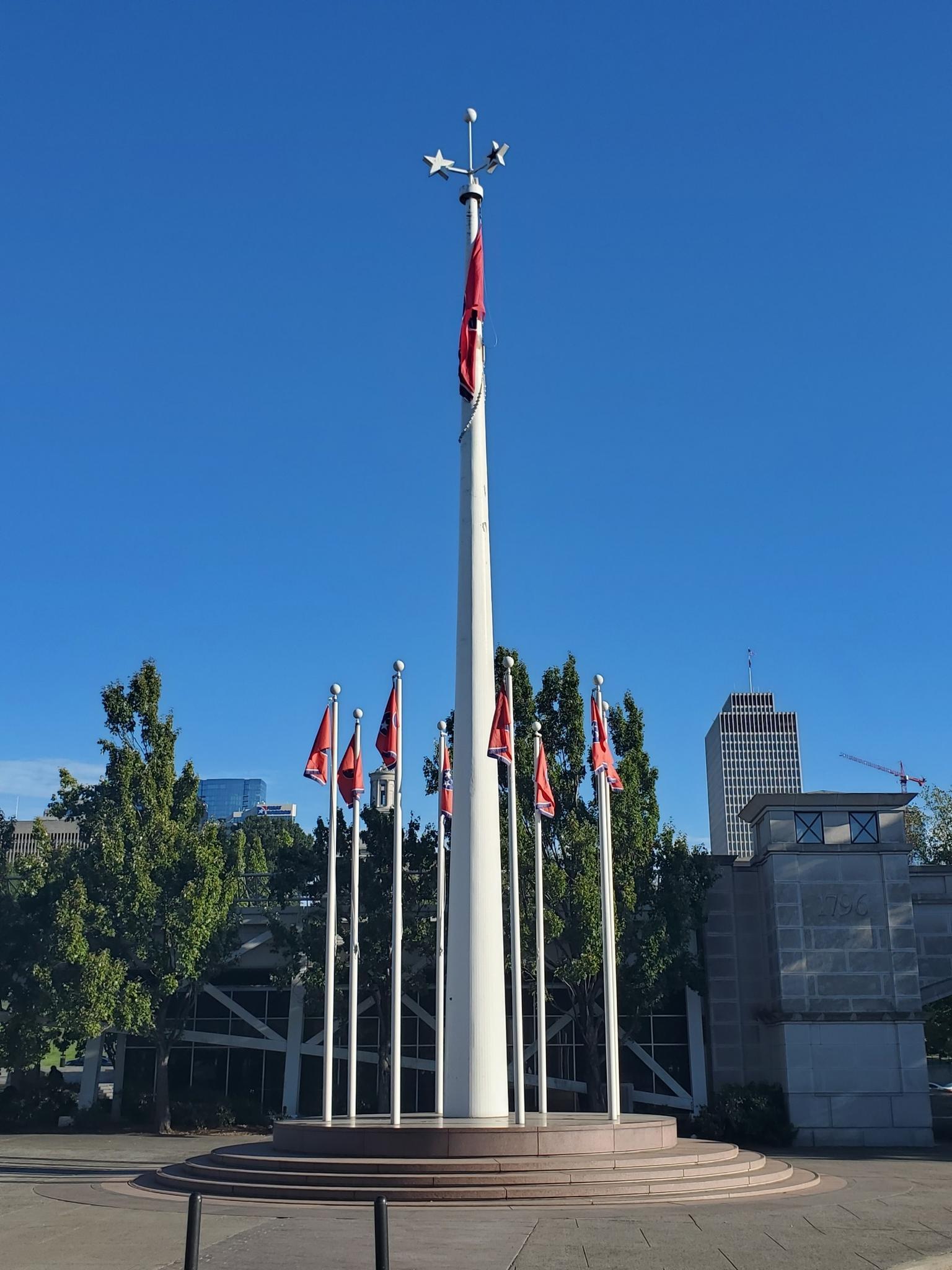 A tall flagpole with a large flag, surrounded by smaller flags on a clear day.