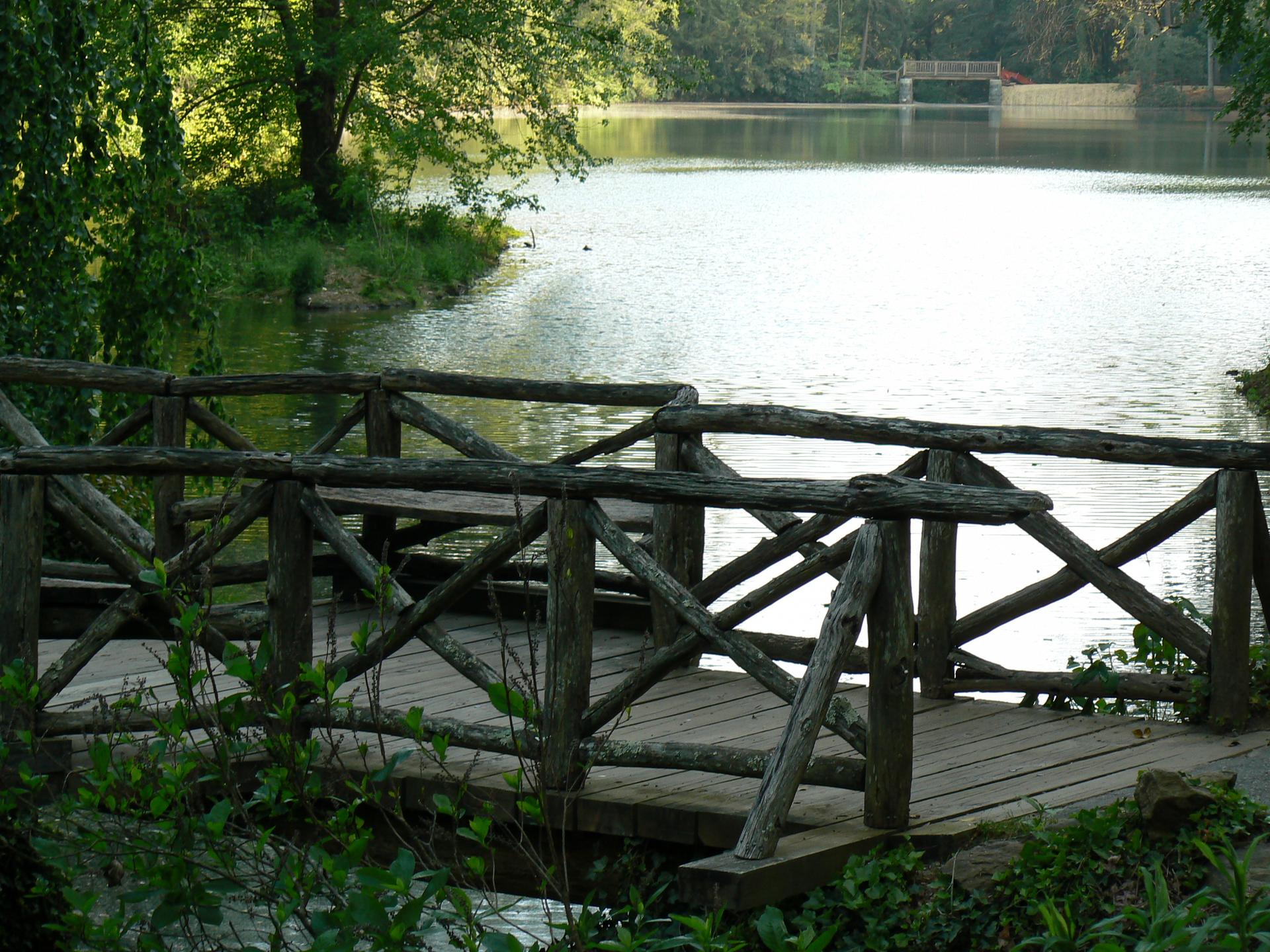 Rustic wooden bridge with railings overlooking a calm lake on a sunny day.