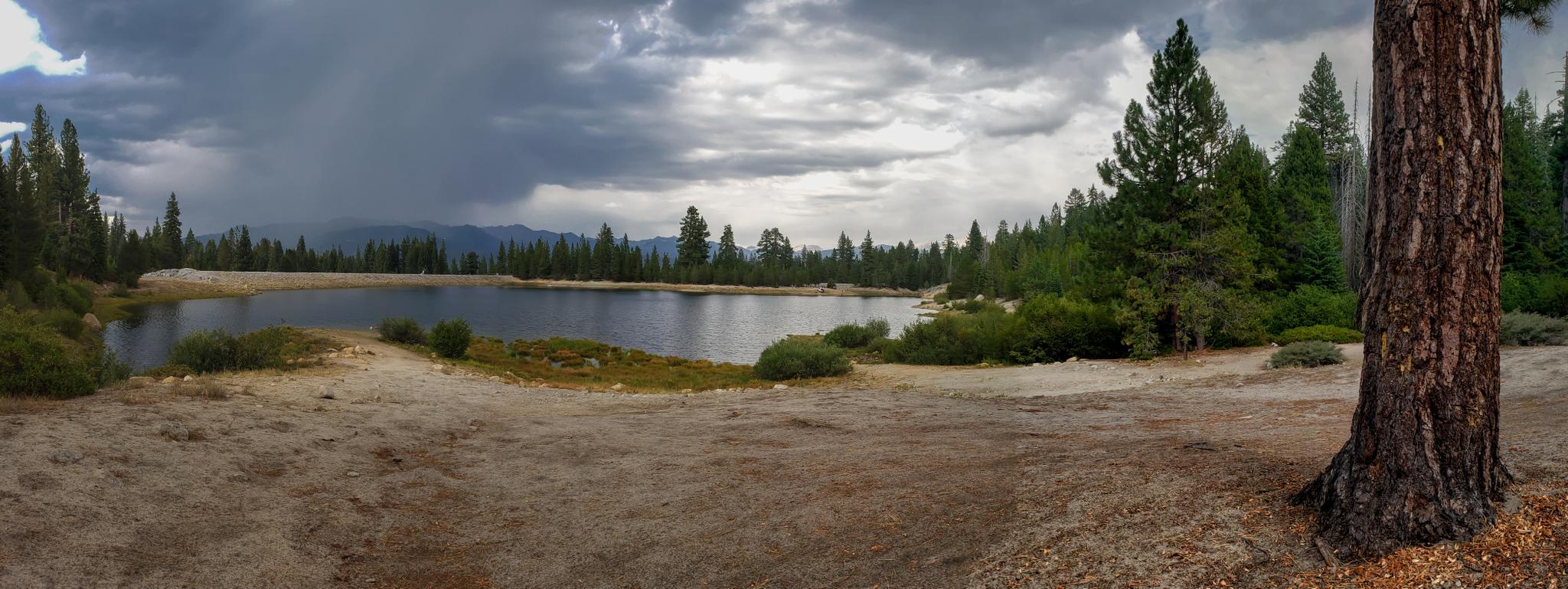 A panoramic view of a lake surrounded by forest under a stormy sky.