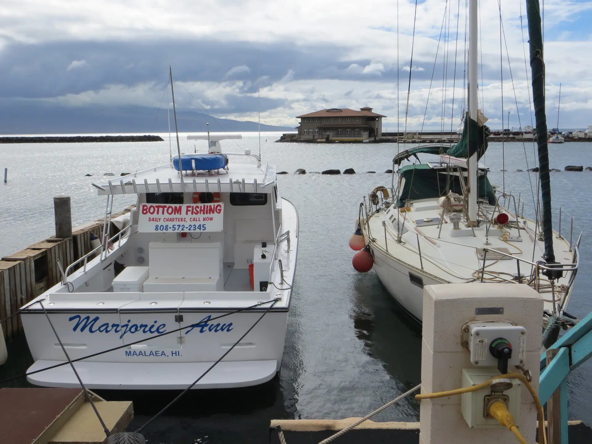 Two boats, a fishing vessel and a sailboat, docked in a calm harbor.