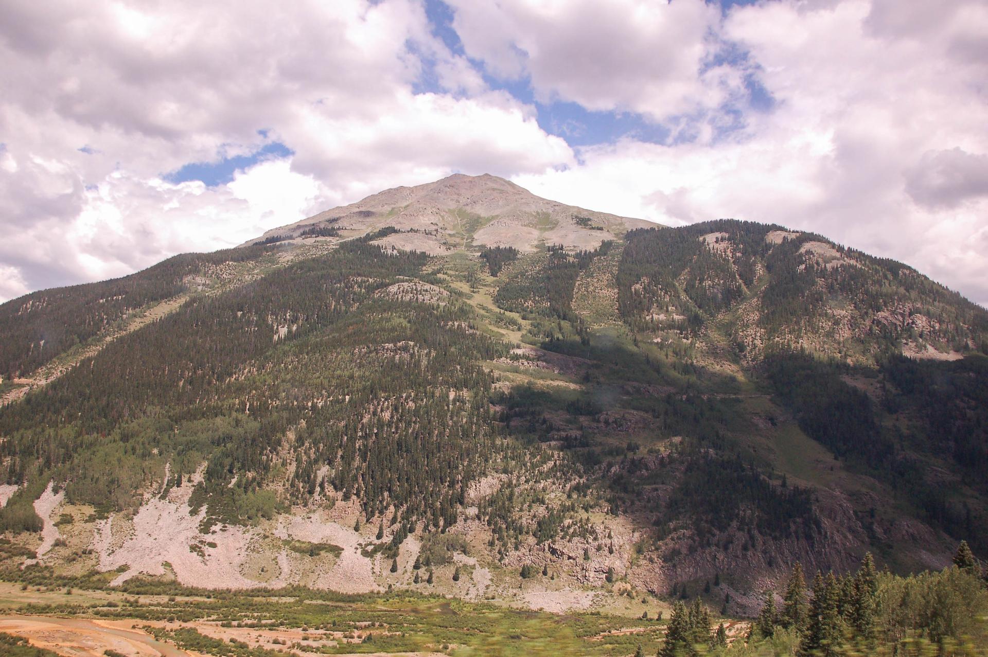 A massive, rocky mountain with green slopes under a partly cloudy sky.