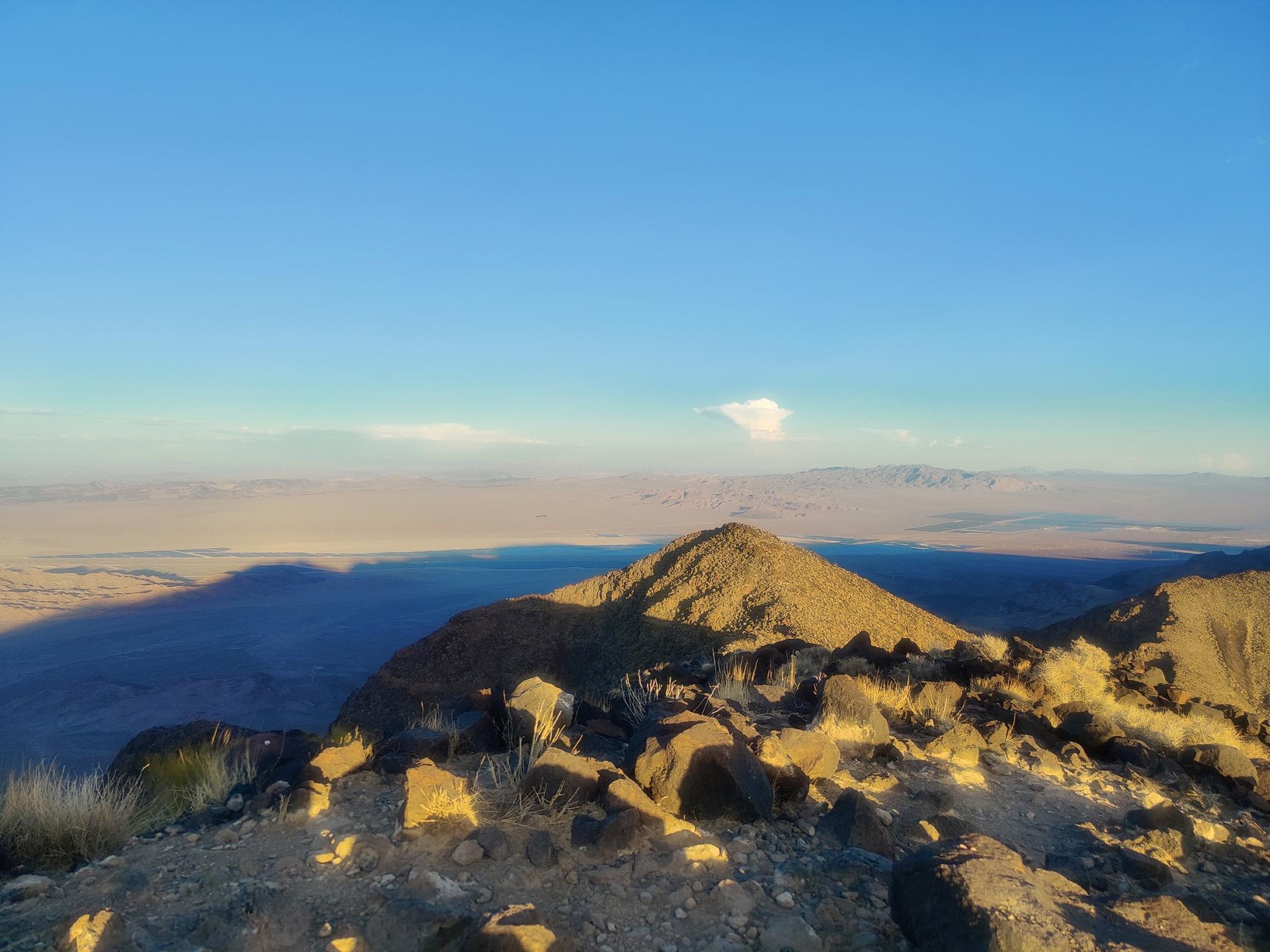 Mountain peak at sunset, casting long shadows over a vast desert landscape.