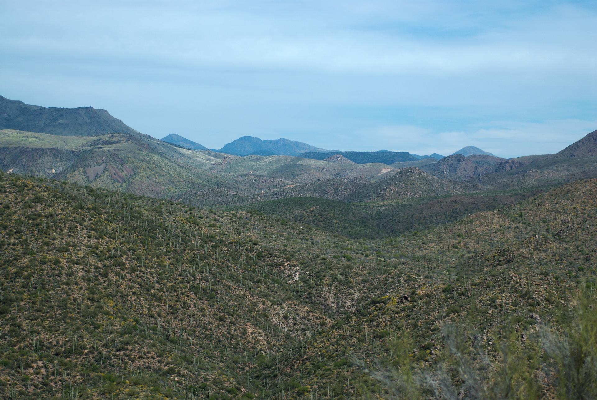 Vast desert valley with green hills and distant blue mountains under a cloudy sky.