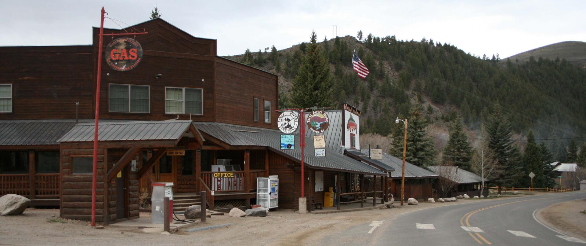 Rustic wooden buildings with a gas sign next to a road, overcast day.