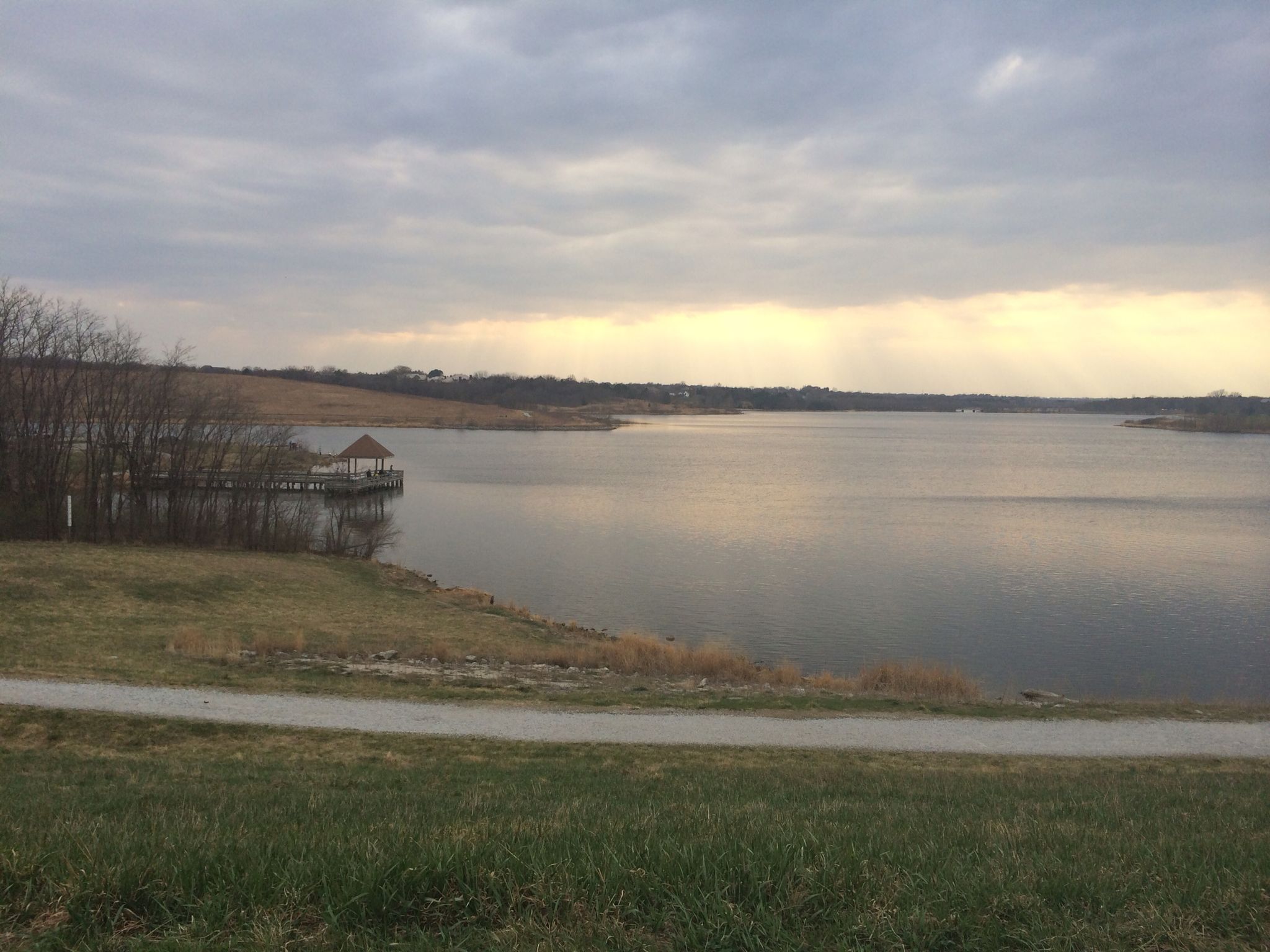 Wide lake with a dock and gazebo under a cloudy, muted sky. - Zorinsky Lake Trail