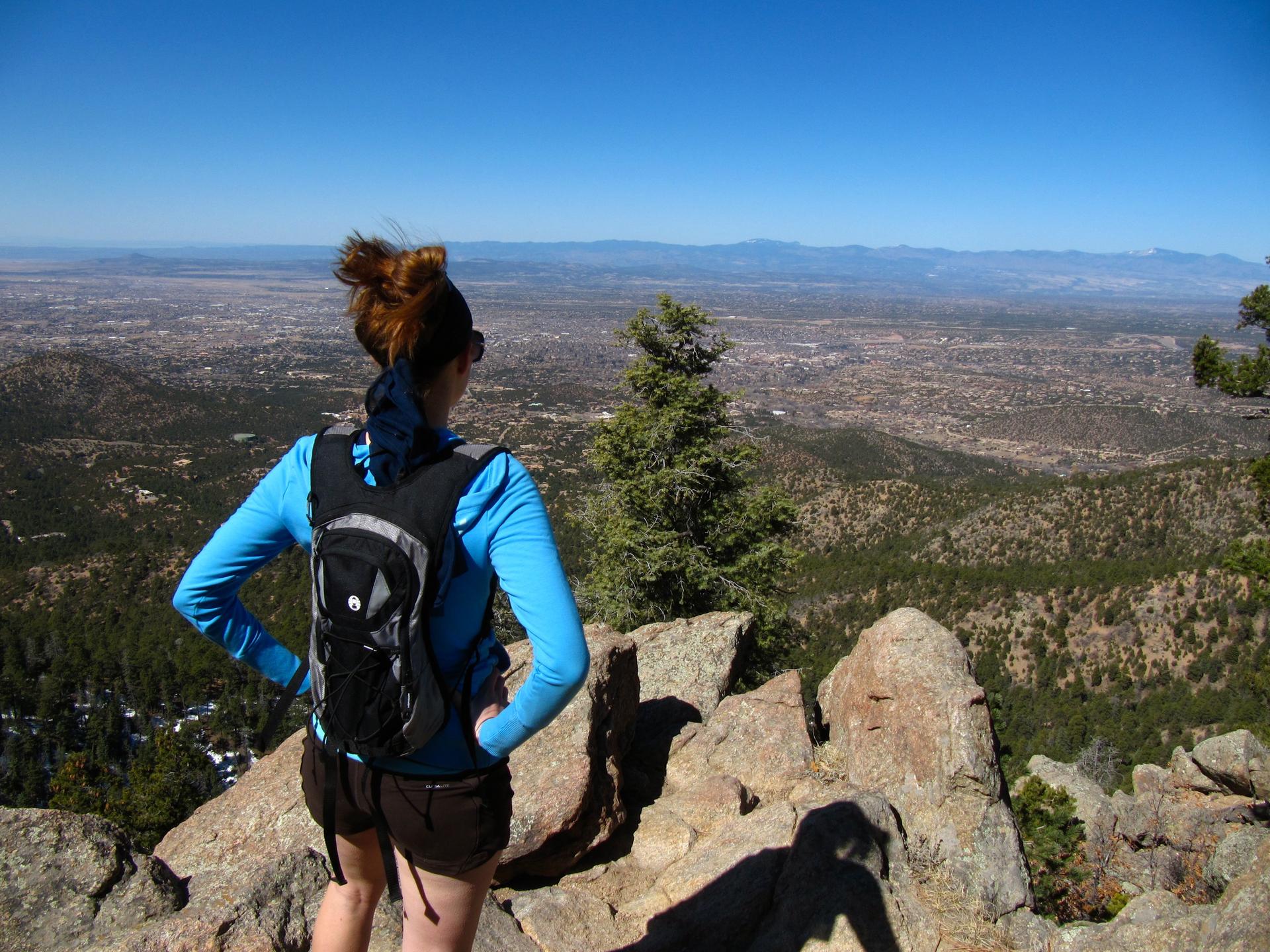 Hiker in blue shirt and backpack overlooking a vast valley on a sunny day.