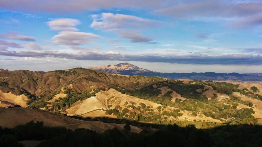 Golden hour light illuminates rolling hills and a distant mountain under dramatic clouds.