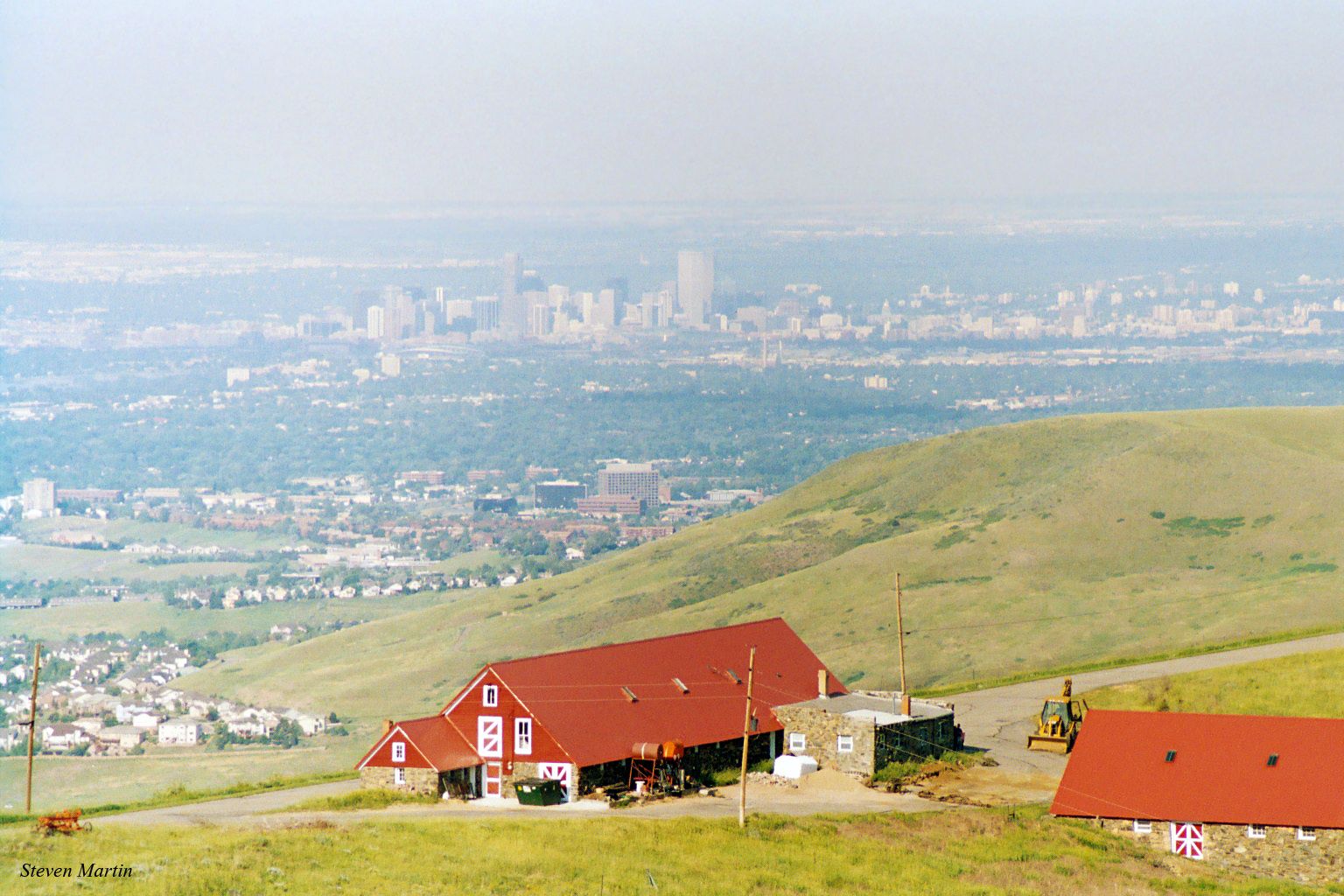 Red buildings on a green hillside overlook a hazy distant city. - Mother Cabrini Shrine Climb