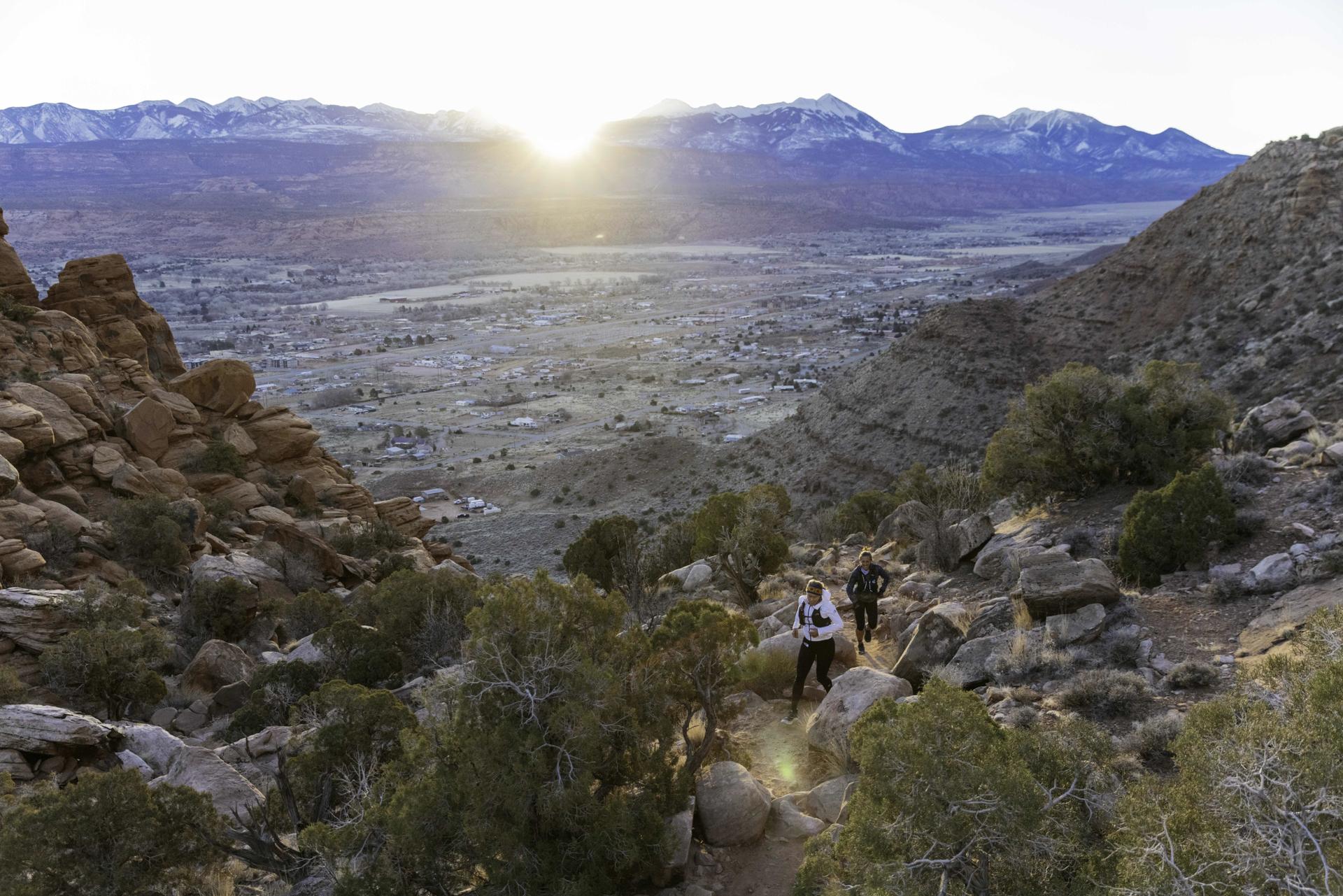 Two hikers on a rocky trail overlooking a valley at sunset.