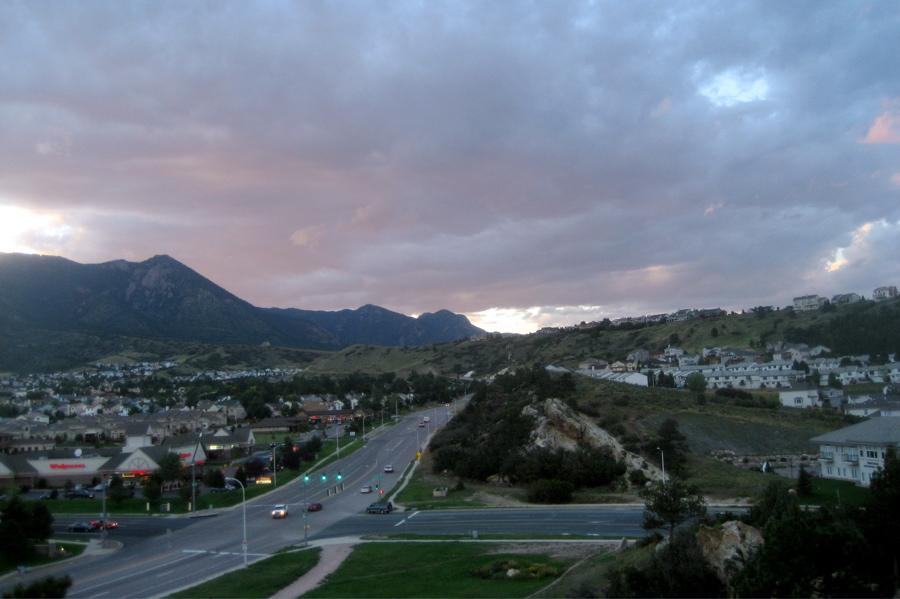 Town nestled in mountains with a road under a dramatic, cloudy sky.