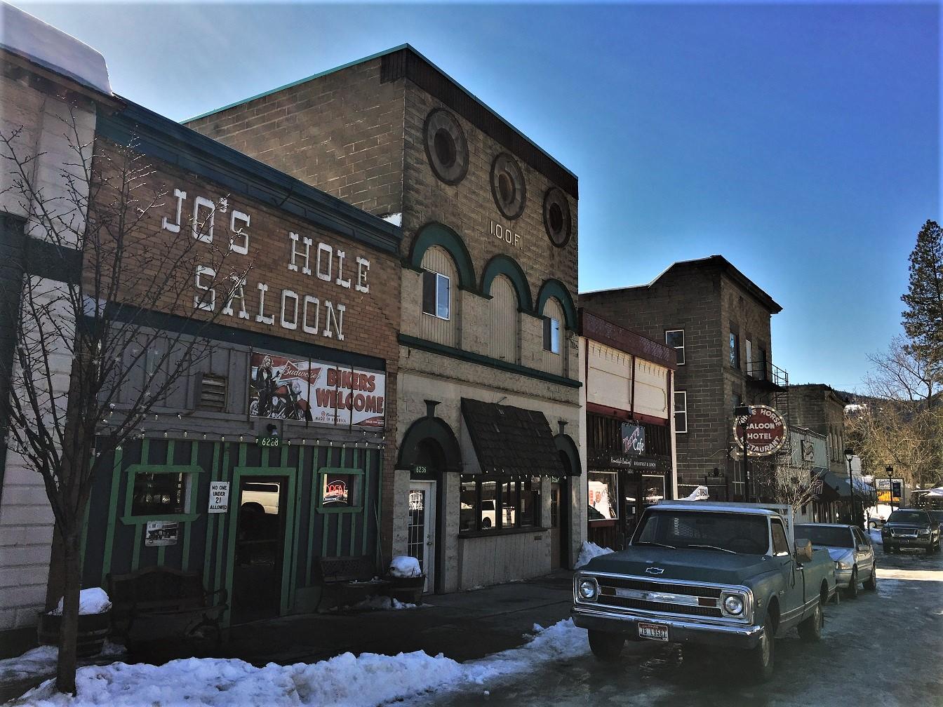 Historic buildings line a snowy street with a vintage truck under blue sky.