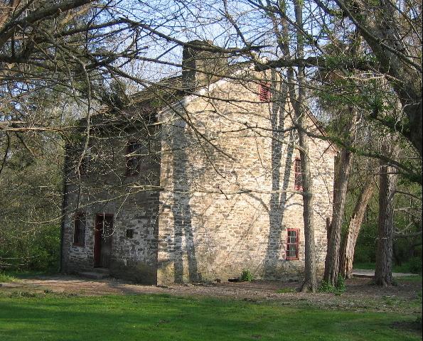 Sunlight illuminates an old stone building with red windows, surrounded by trees.