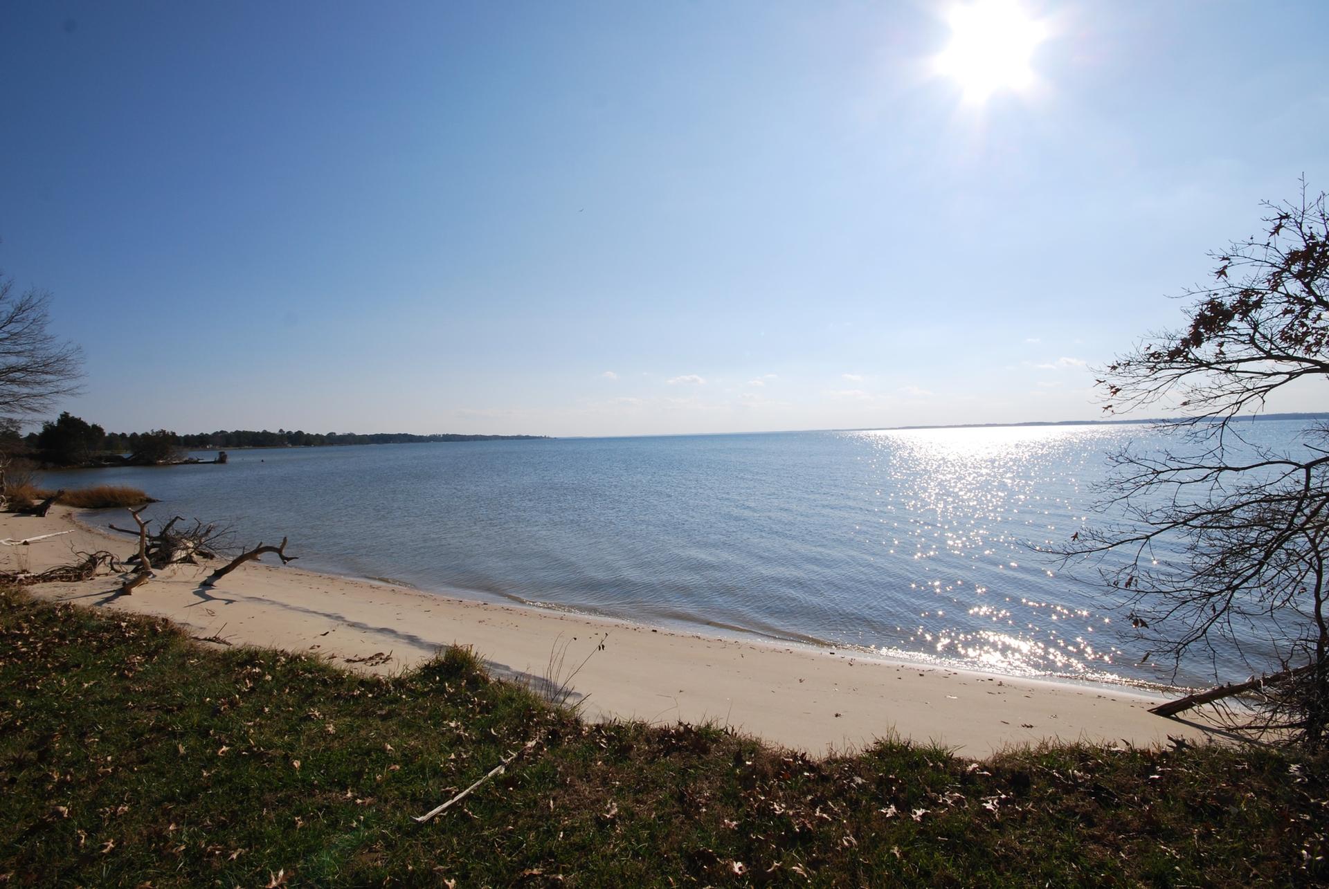 Sunny beach with calm water, bright sun reflecting on the surface.