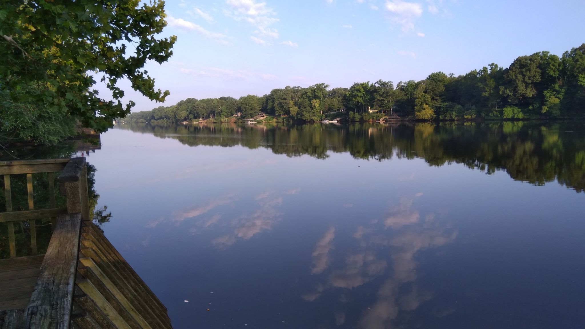 A calm river reflects the sky, bordered by green trees and a wooden dock. - Sanders Ferry Ride