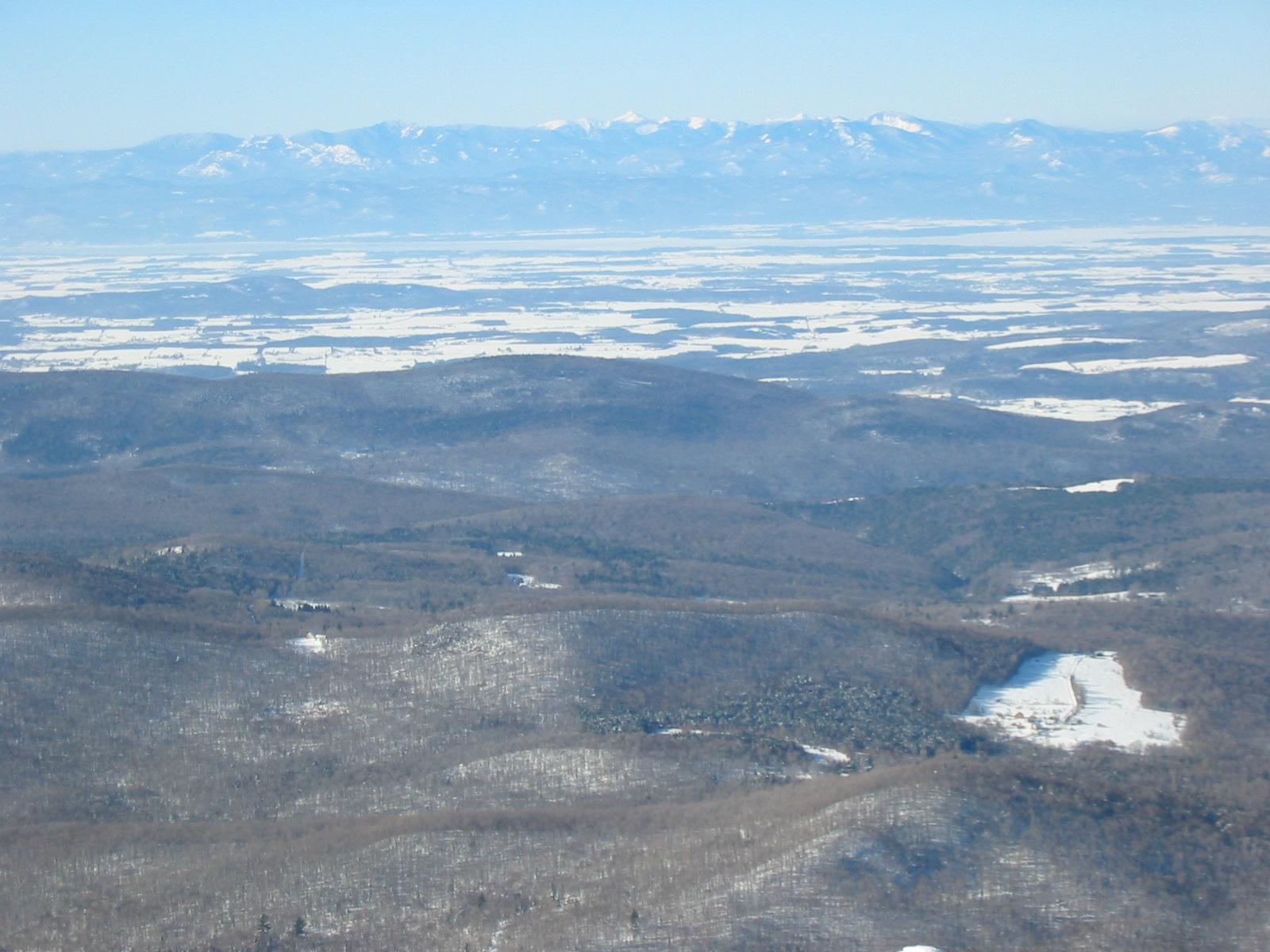 Expansive winter landscape with snow-covered hills and distant mountain range.