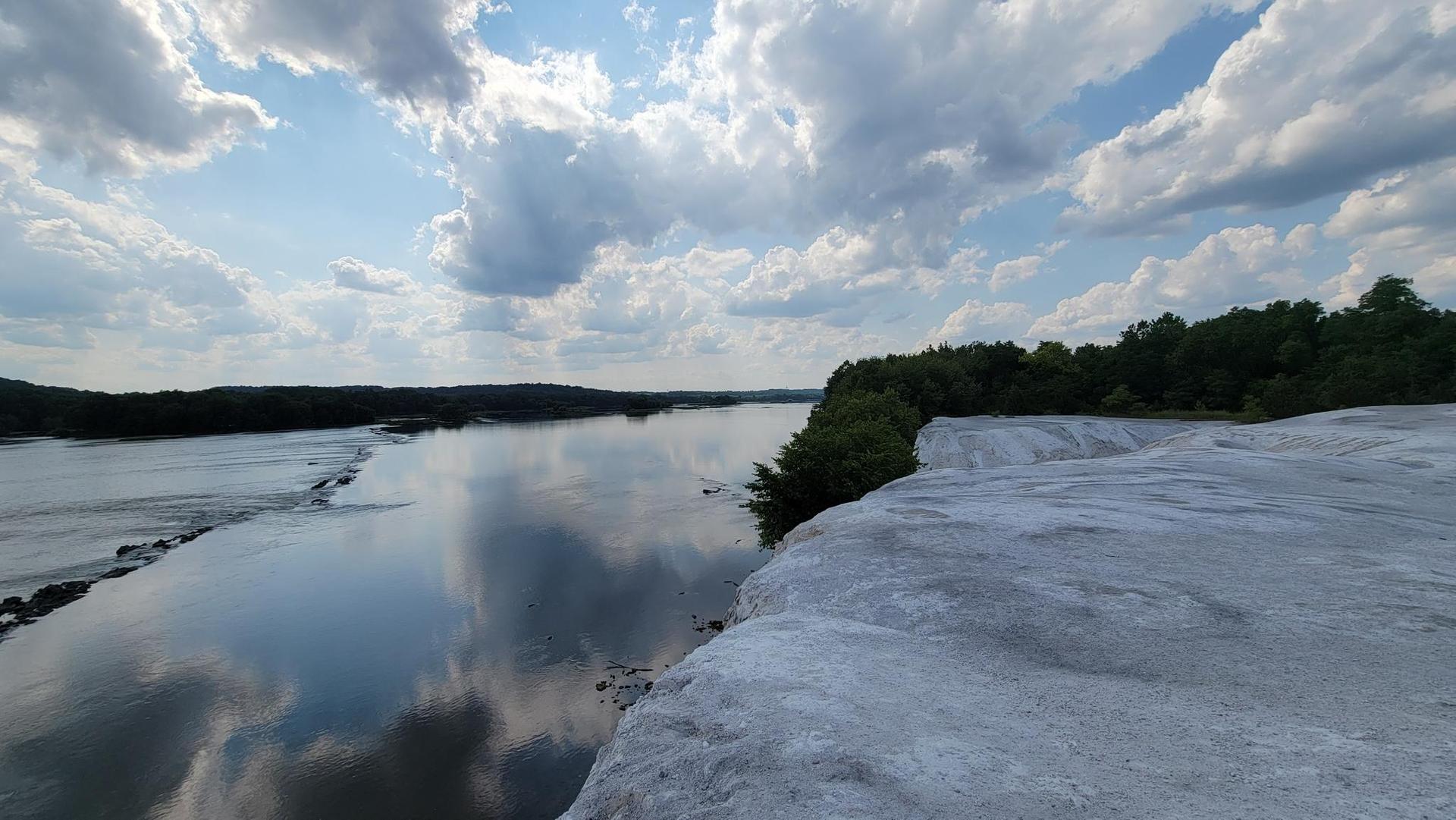 Wide river reflects a cloudy sky, seen from a white rocky cliff edge.