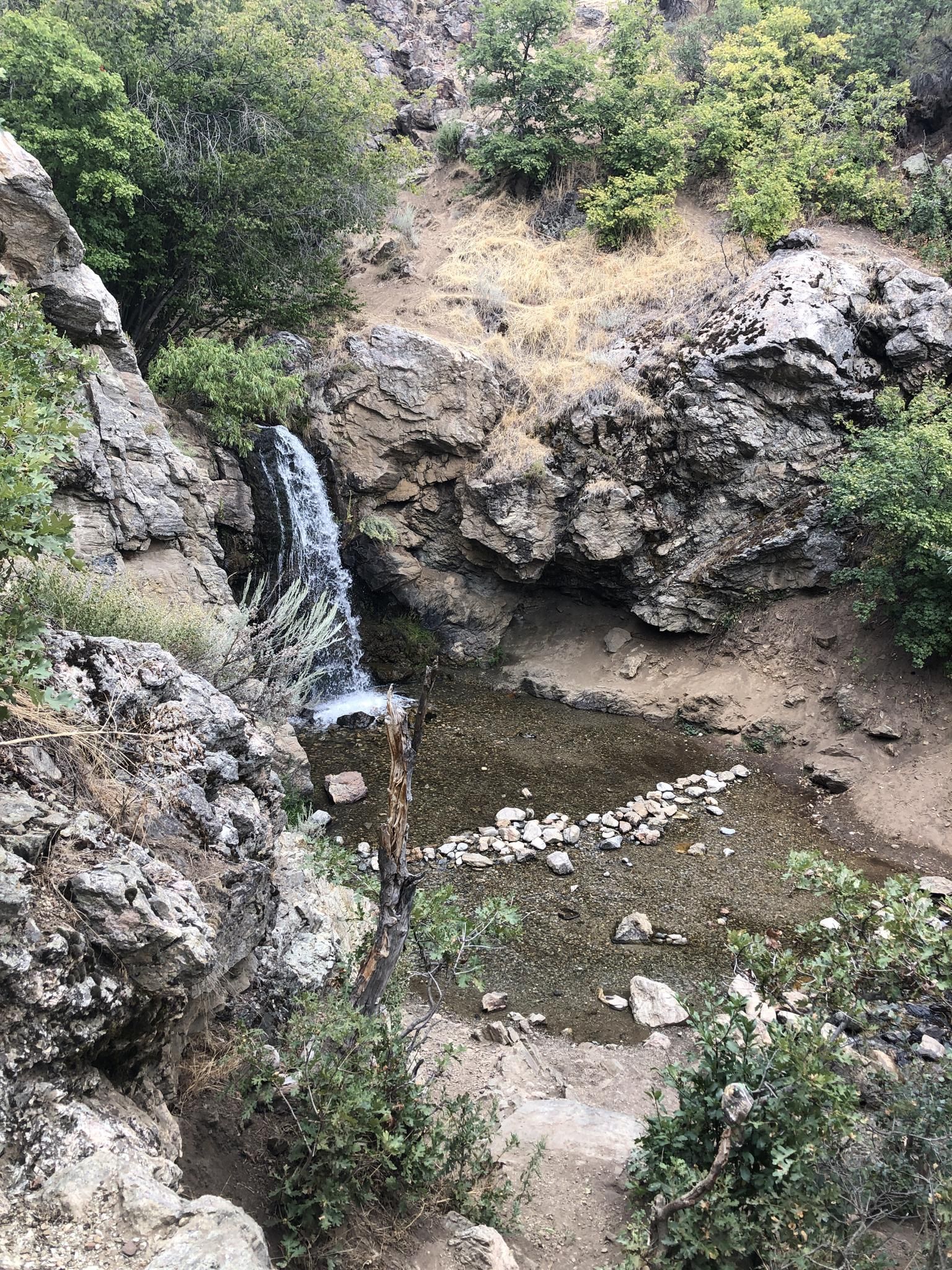 Waterfall cascading into a rocky pool, surrounded by green and dry vegetation. - Adam’s Canyon Lower Falls
