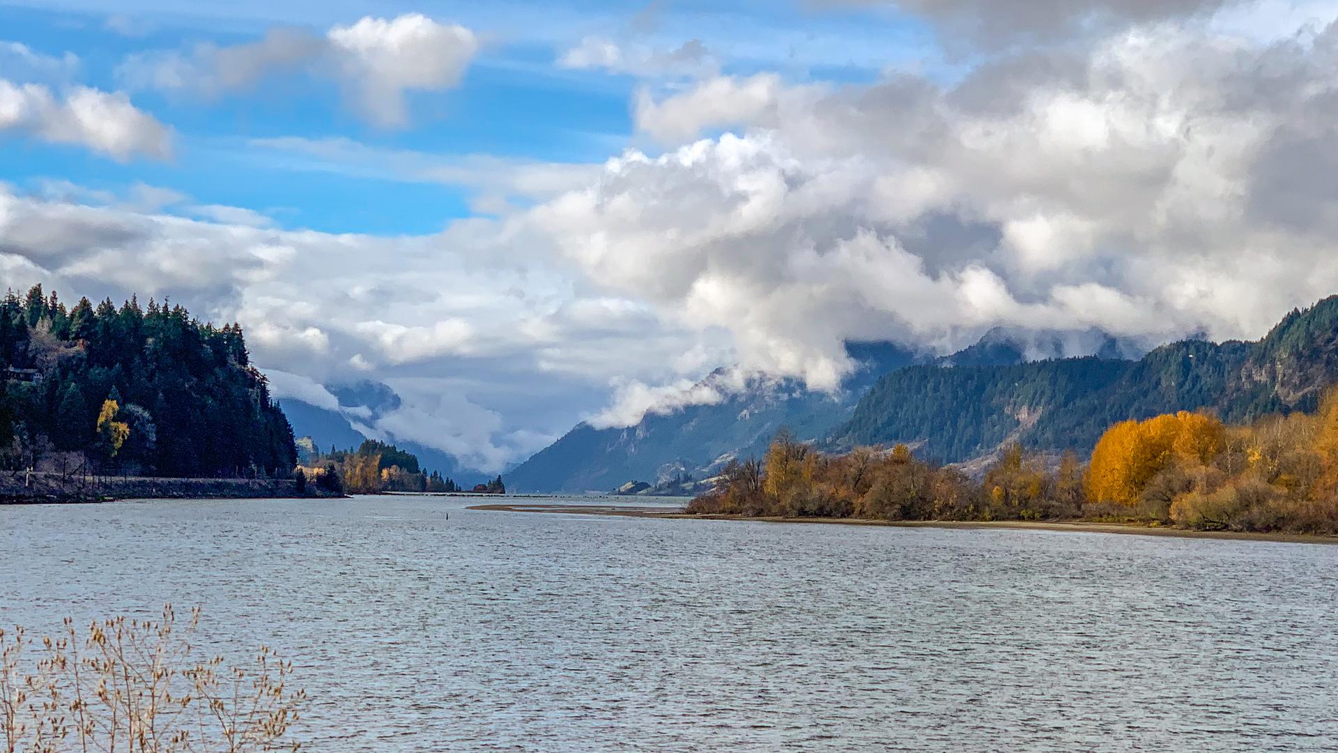 Wide river flowing through a valley with forested mountains and autumn trees.
