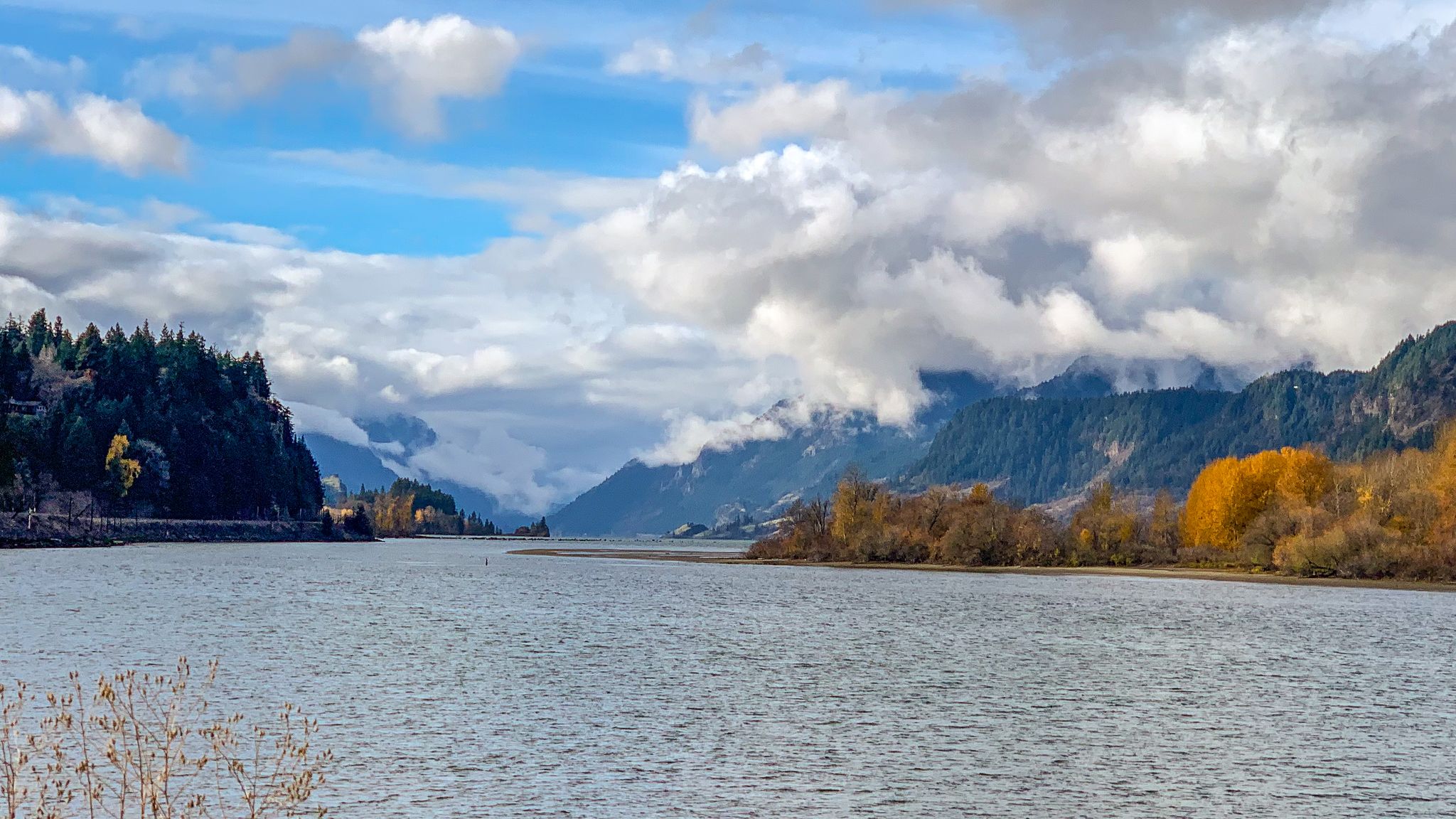 Wide river flowing through a valley with forested mountains and autumn trees. - Hood River Waterfront