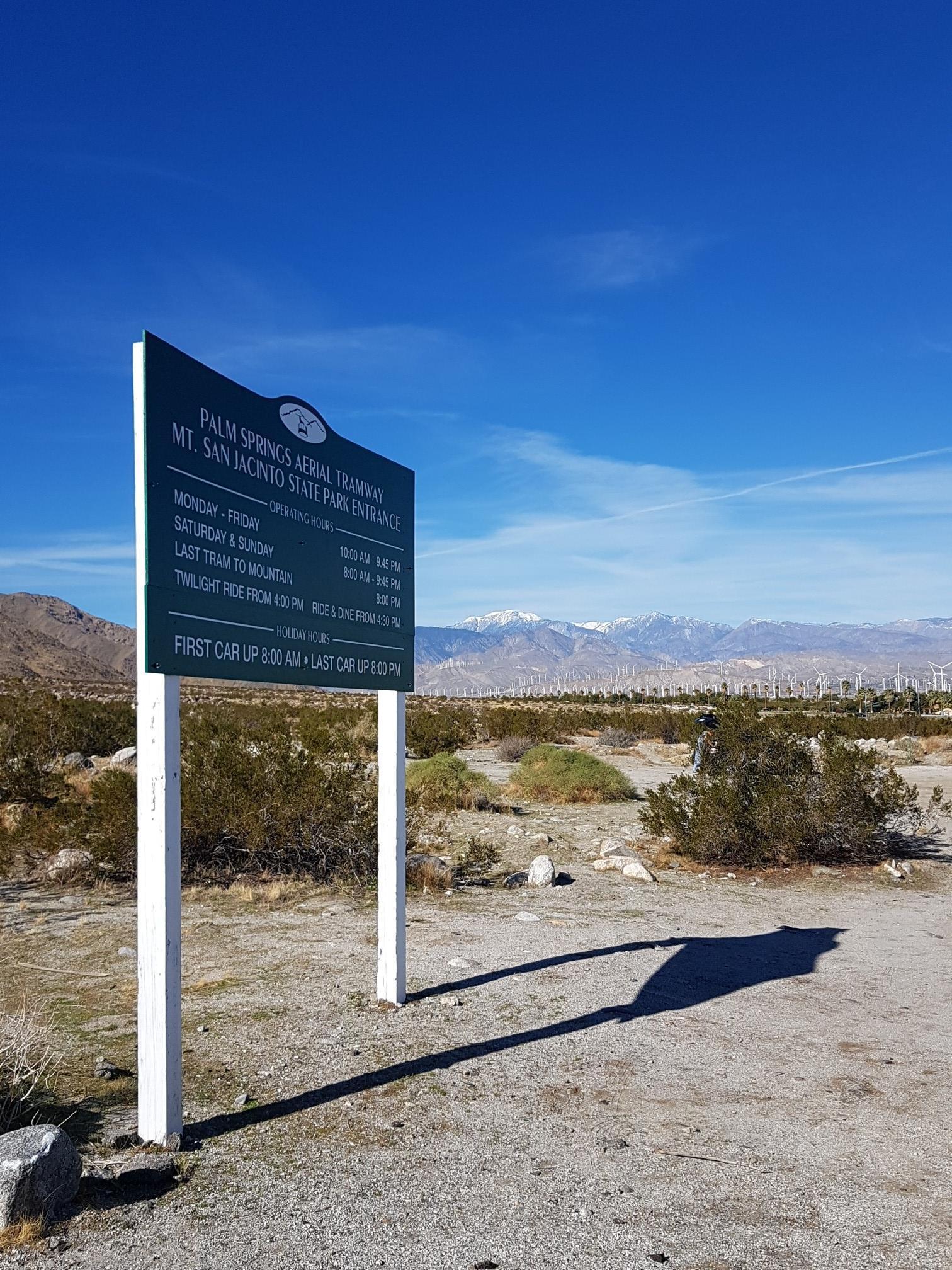 A large green sign stands in a sunny desert landscape with distant mountains.